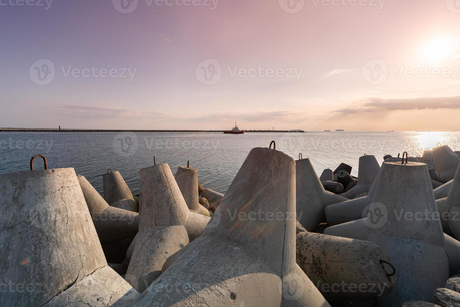 Tugboat sailing in sea to tow ship to port. Tetrapod breakwaters in harbor. Beautiful sunset over the pier. photo