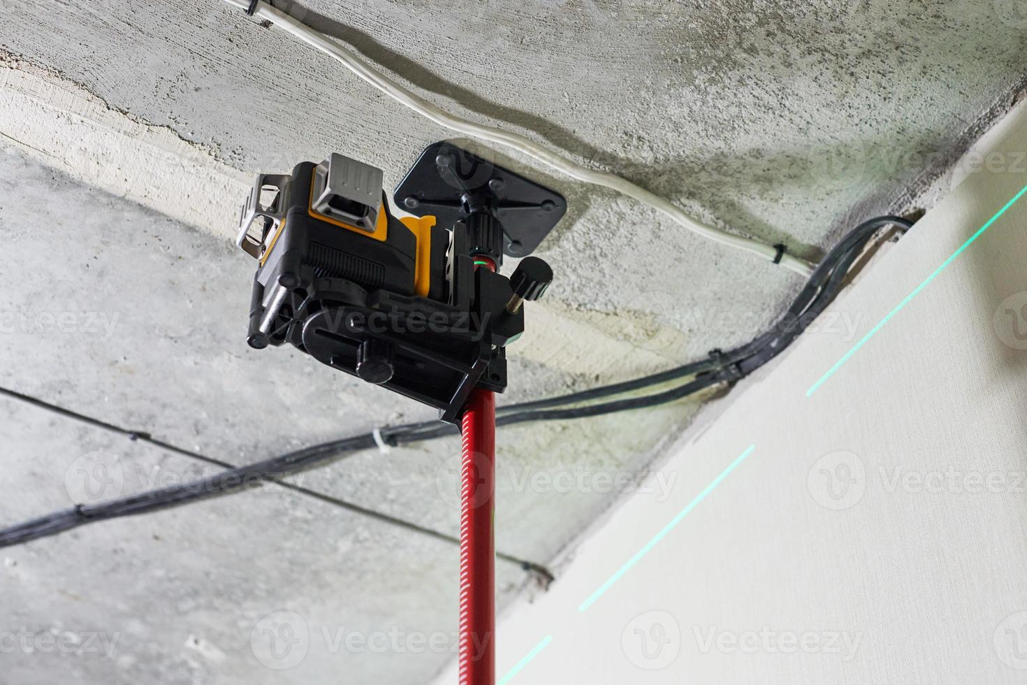 Laser level measuring tool with visible green laser beam on wall for installing stretch ceiling photo