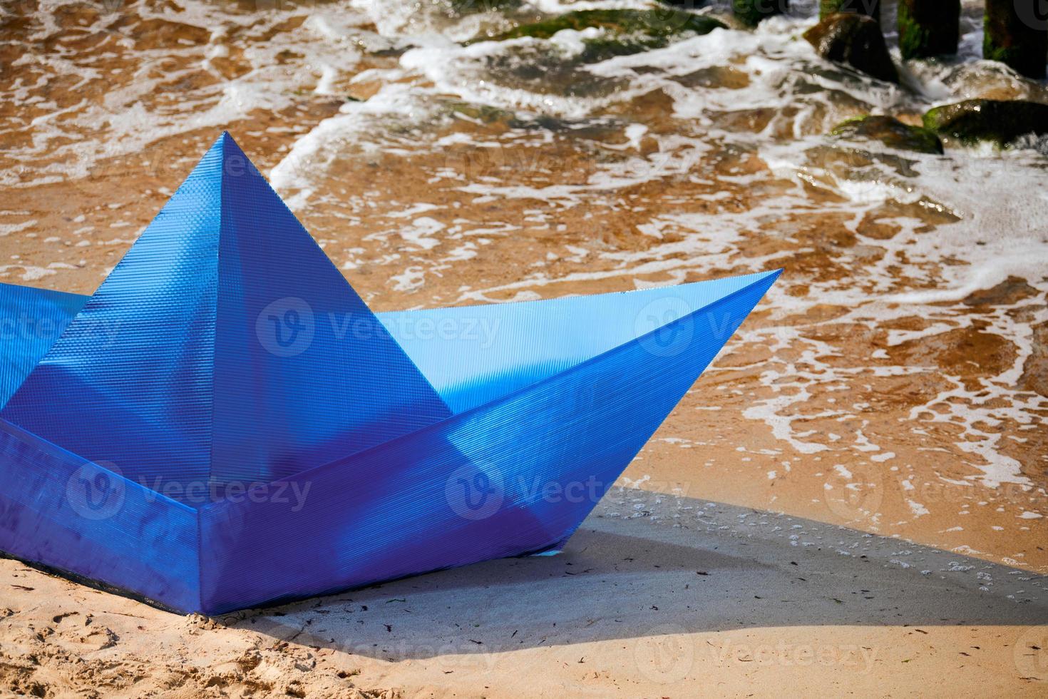 Origami blue paper boat on sandy beach for concept design, beautiful paper ship on shore, close up photo