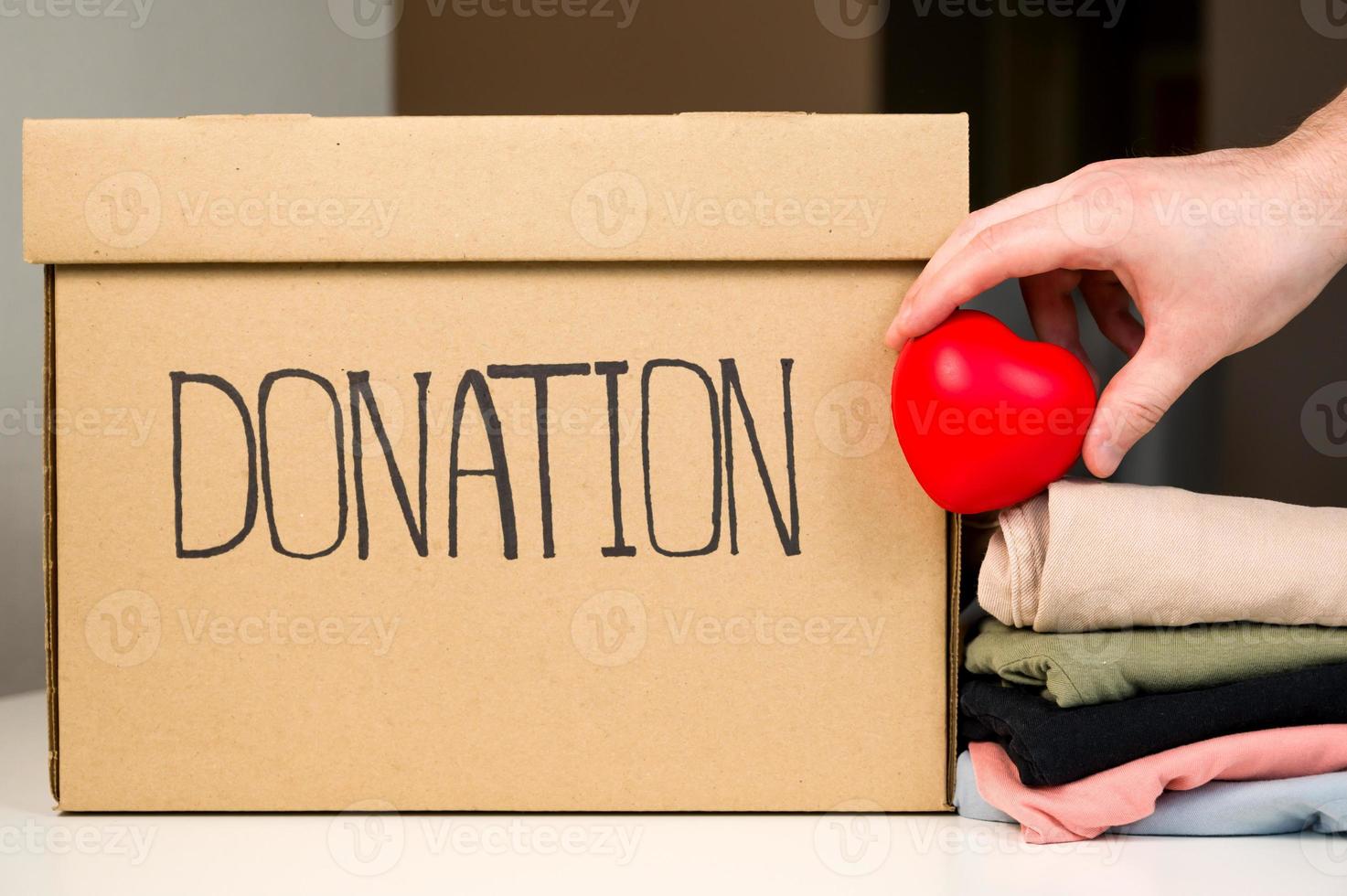 Unrecognizable male holding heart near donation box and stack of clothes. Helping people. Charity photo