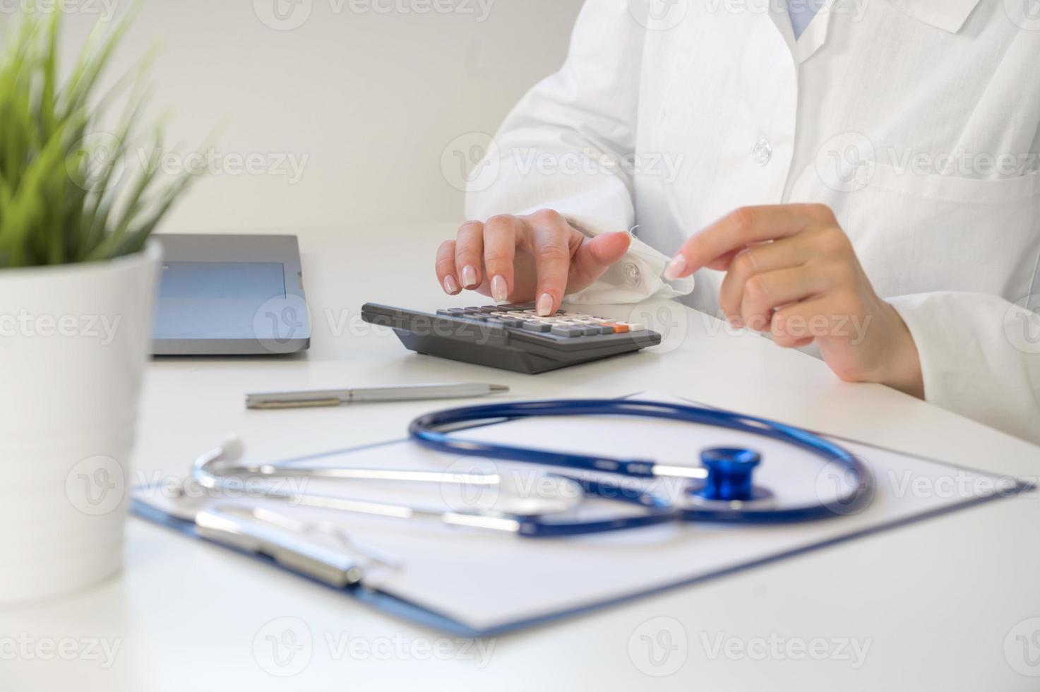 Medical insurance concept . Unrecognizable doctor or nurse with calculator at the table with stethoscope and forms photo