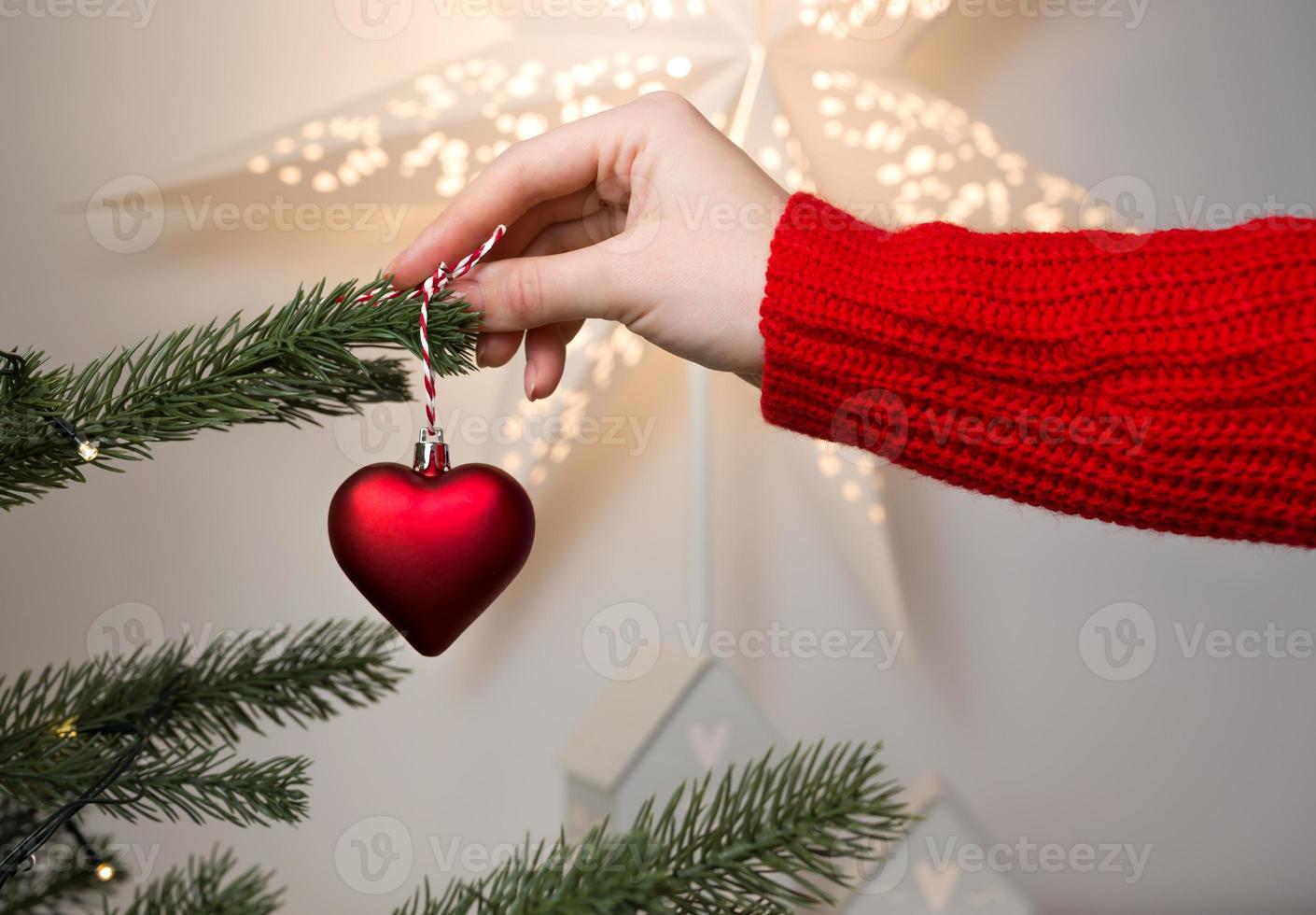 closeup of Female hands holding Christmas ornament heart shape for decorating fir tree. Winter holidays banner photo