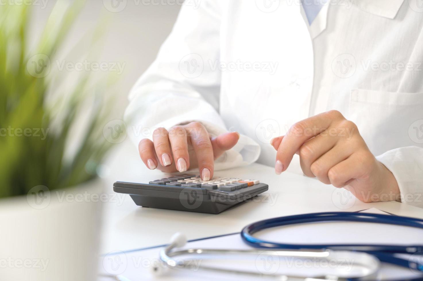 Medical insurance concept . Unrecognizable doctor or nurse with calculator at the table with stethoscope and forms photo