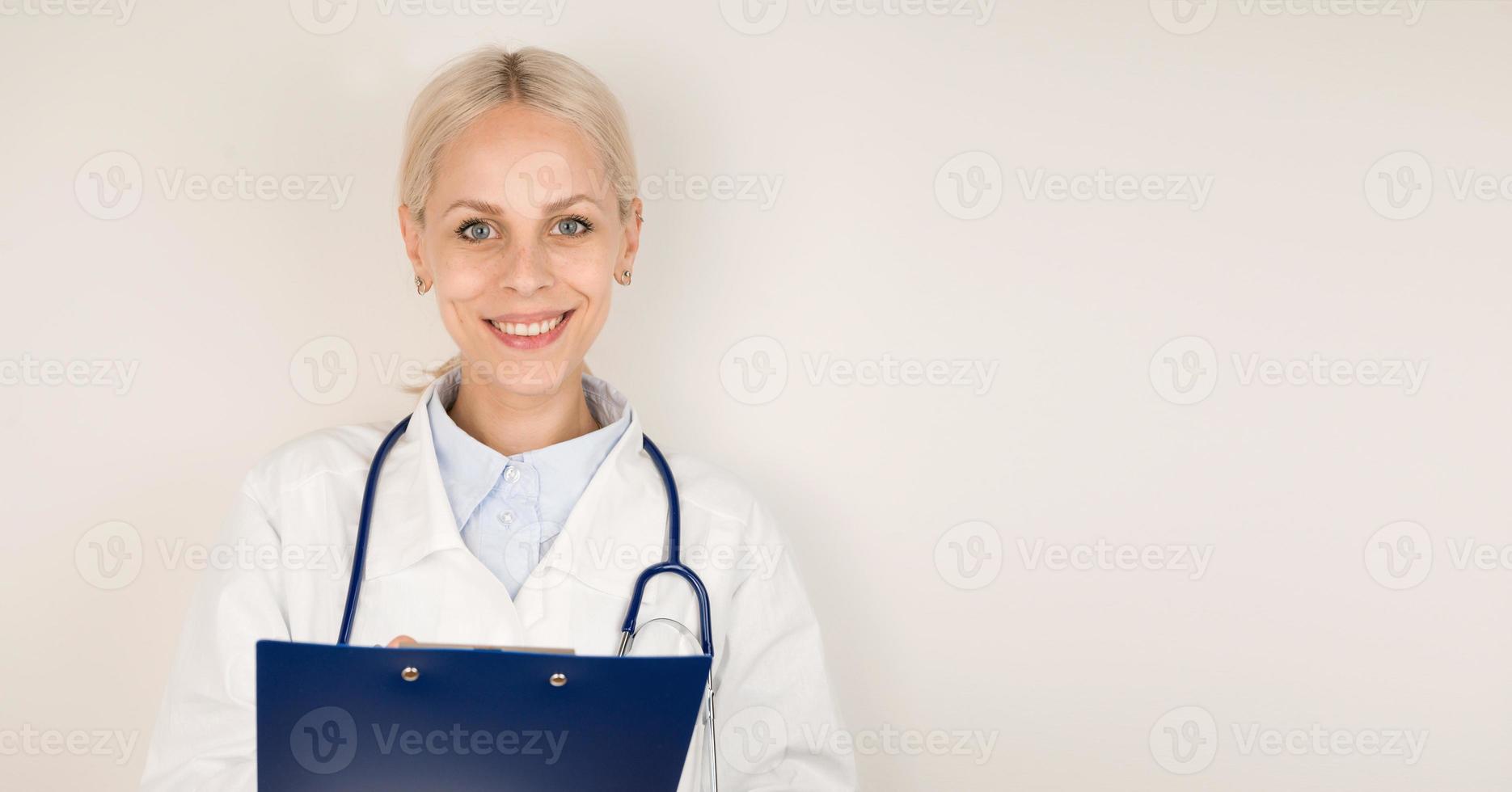 Young happy female doctor in medical coat with stethoscope smiling with tablet in her hands.Copy space banner photo