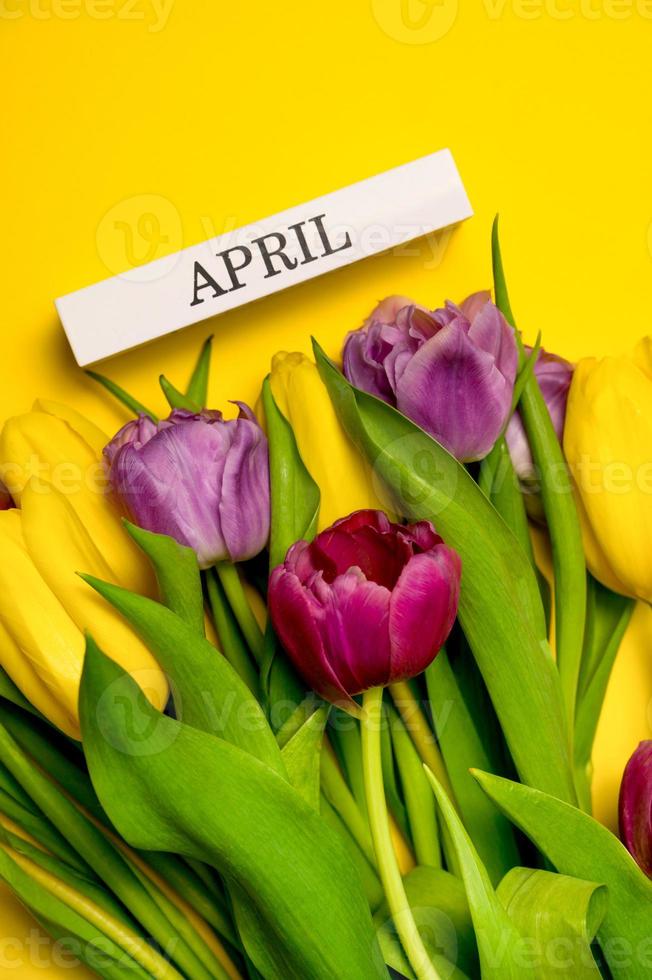 Vertical Easter card with tulips and april written on wooden block. photo