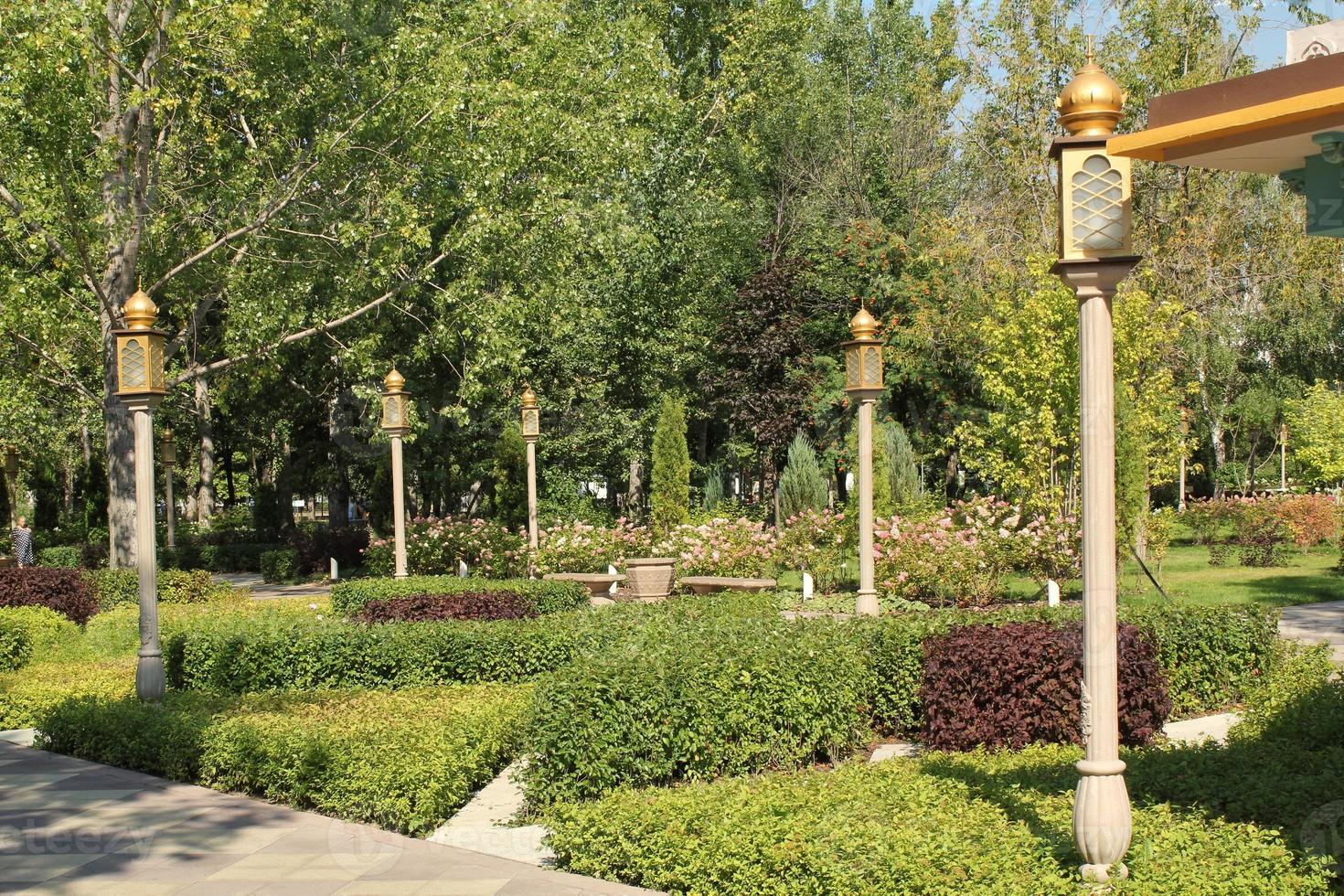 Trees and flowers in city park with Indian style lantern. Pedestrian zone for walking. Urban planning, public space concept. Town recreation area. Architecture design comfortable garden. Footpath way photo