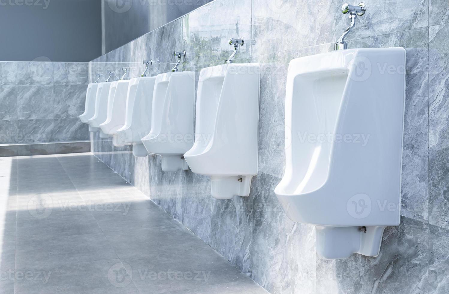 Men's room with white porcelain urinals in line in gas station photo