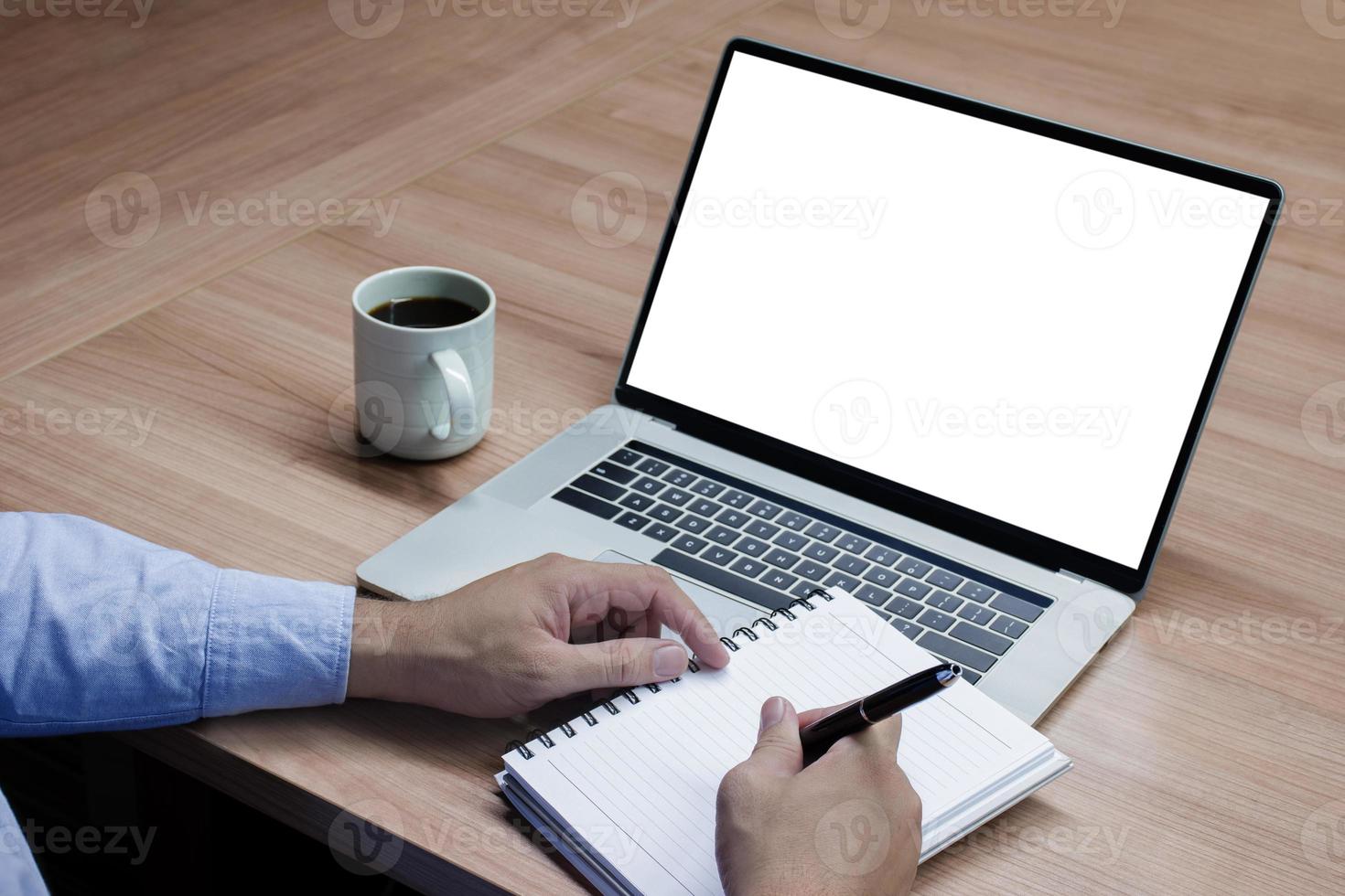 Businessman hand holding a pen to paperwork with white screen background mock up on display laptop with clipping path photo