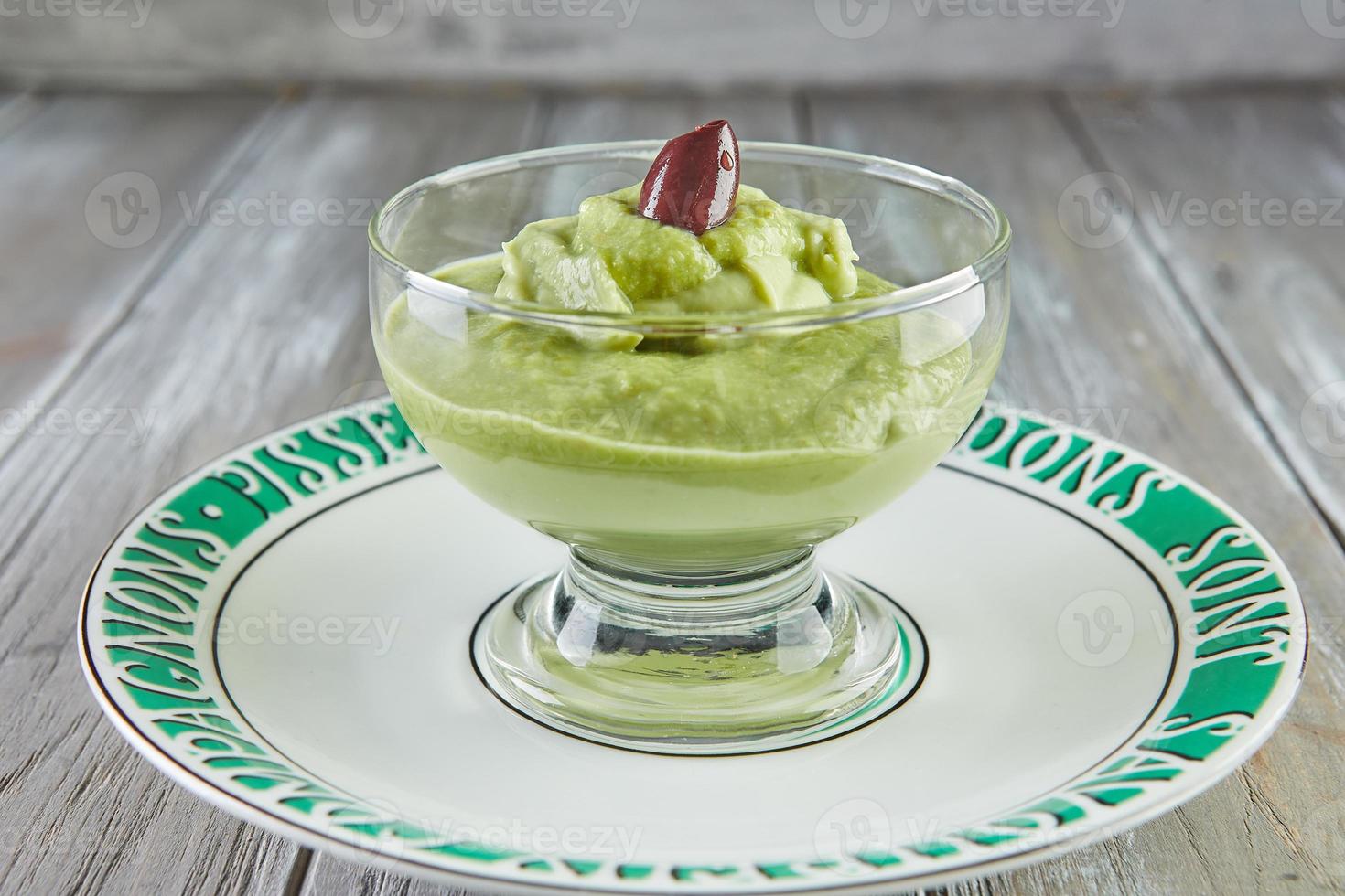 Avocado mousse with olives in transparent glass cup, on plate photo