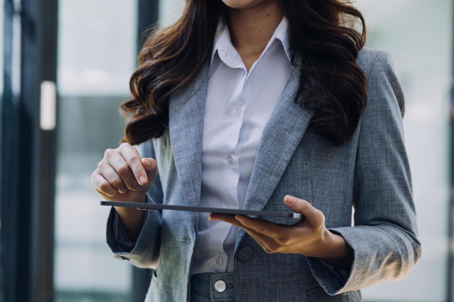Young business woman sitting in office at table and using smartphone. On desk is laptop and tablet computer, on screen charts and graphs. Woman analyzing data. Student learning online. photo