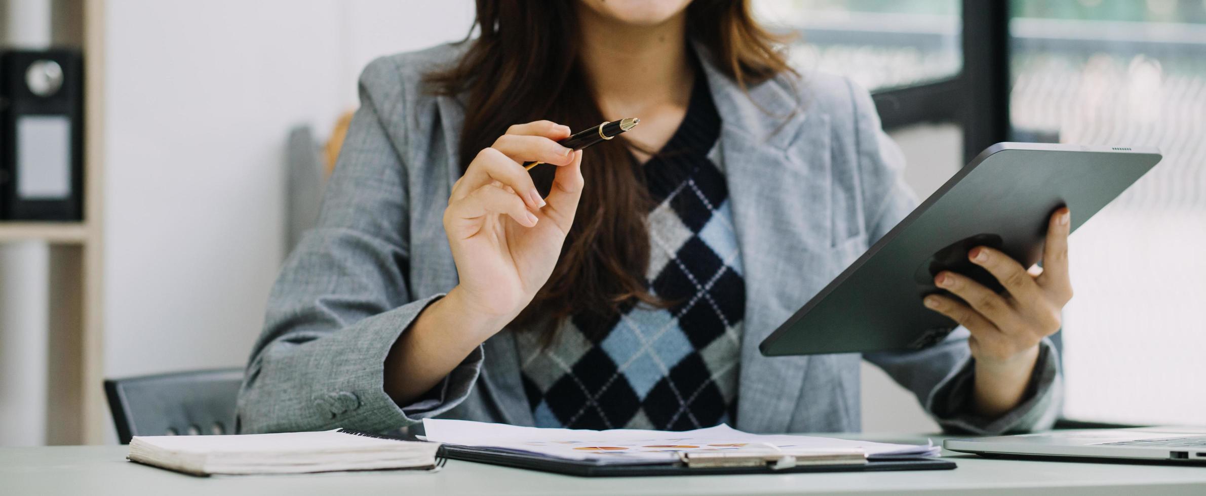 Young business woman sitting in office at table and using smartphone. On desk is laptop and tablet computer, on screen charts and graphs. Woman analyzing data. Student learning online. photo