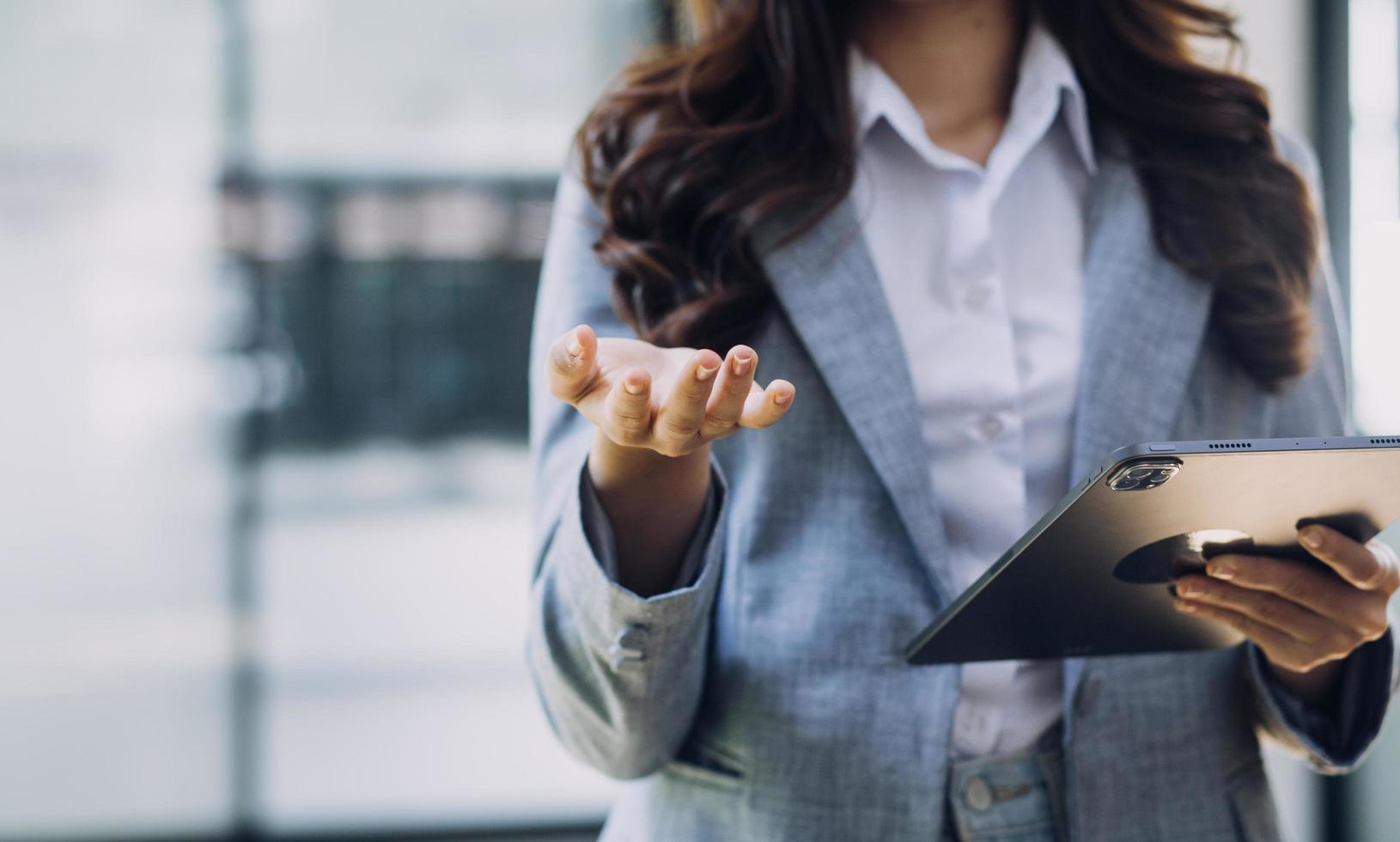 Young business woman sitting in office at table and using smartphone. On desk is laptop and tablet computer, on screen charts and graphs. Woman analyzing data. Student learning online. photo