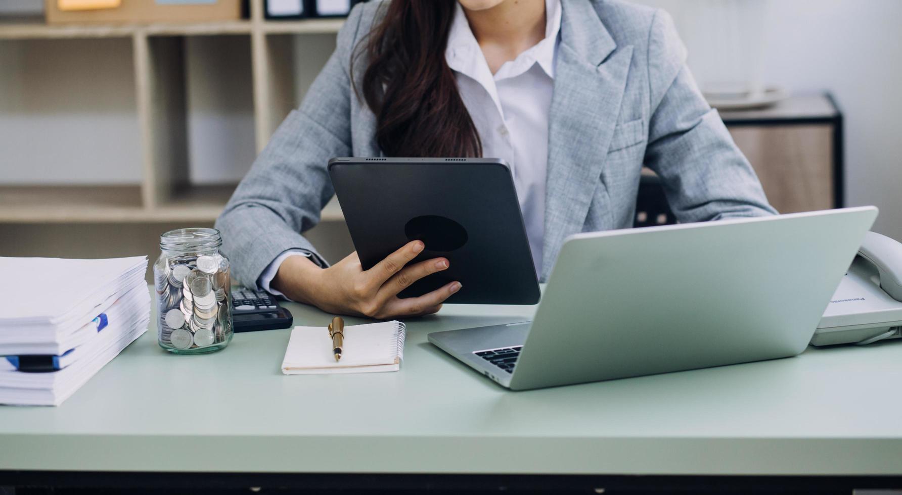 Young business woman sitting in office at table and using smartphone. On desk is laptop and tablet computer, on screen charts and graphs. Woman analyzing data. Student learning online. photo