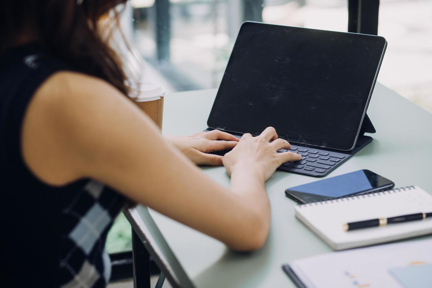 Young business woman sitting in office at table and using smartphone. On desk is laptop and tablet computer, on screen charts and graphs. Woman analyzing data. Student learning online. photo