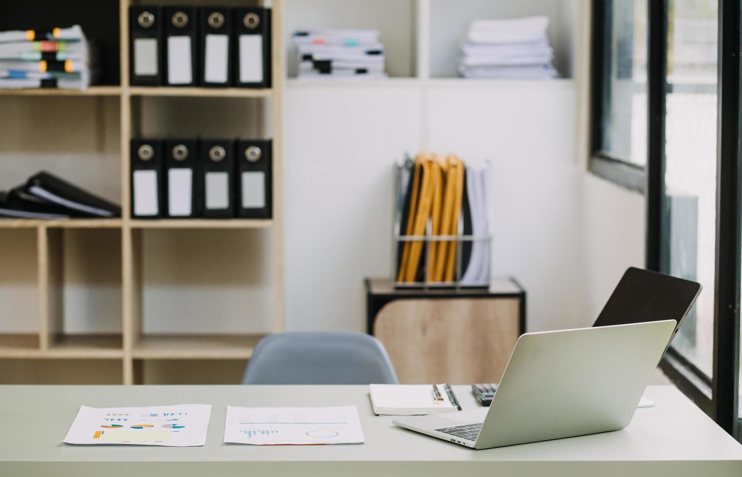 Young business woman sitting in office at table and using smartphone. On desk is laptop and tablet computer, on screen charts and graphs. Woman analyzing data. Student learning online. photo