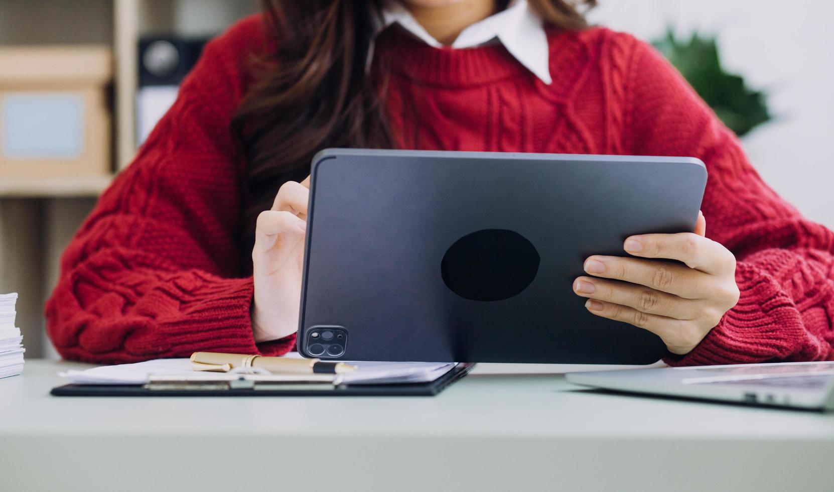 Young business woman sitting in office at table and using smartphone. On desk is laptop and tablet computer, on screen charts and graphs. Woman analyzing data. Student learning online. photo
