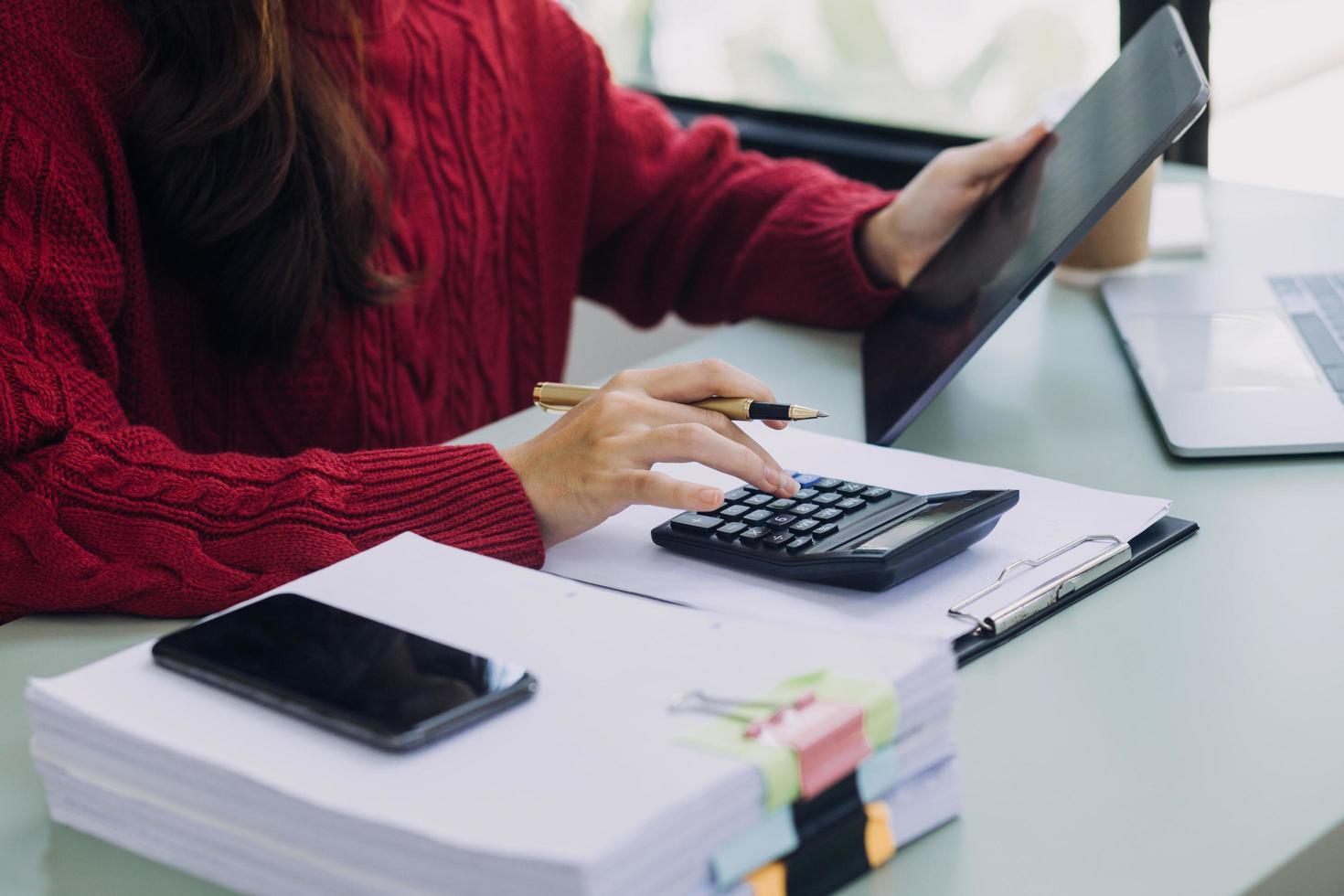 Young business woman sitting in office at table and using smartphone. On desk is laptop and tablet computer, on screen charts and graphs. Woman analyzing data. Student learning online. photo