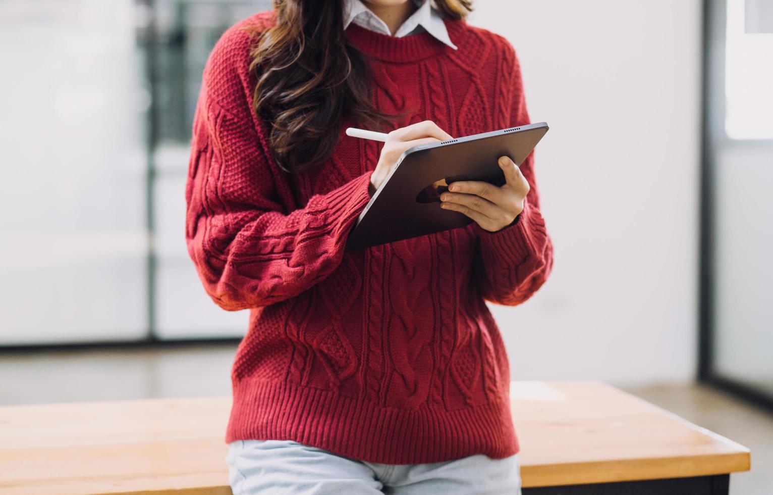 Young business woman sitting in office at table and using smartphone. On desk is laptop and tablet computer, on screen charts and graphs. Woman analyzing data. Student learning online. photo