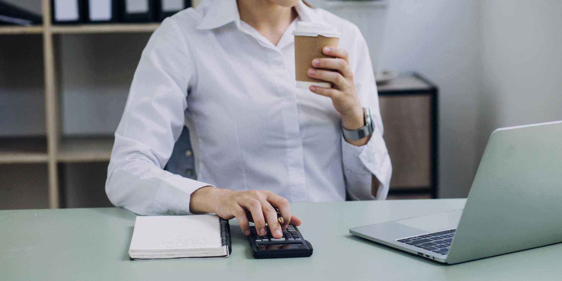 mujer de negocios joven sentada en la oficina en la mesa y usando un teléfono inteligente. en el escritorio hay una computadora portátil y una tableta, en gráficos y gráficos en pantalla. mujer analizando datos. estudiante aprendiendo en línea. foto