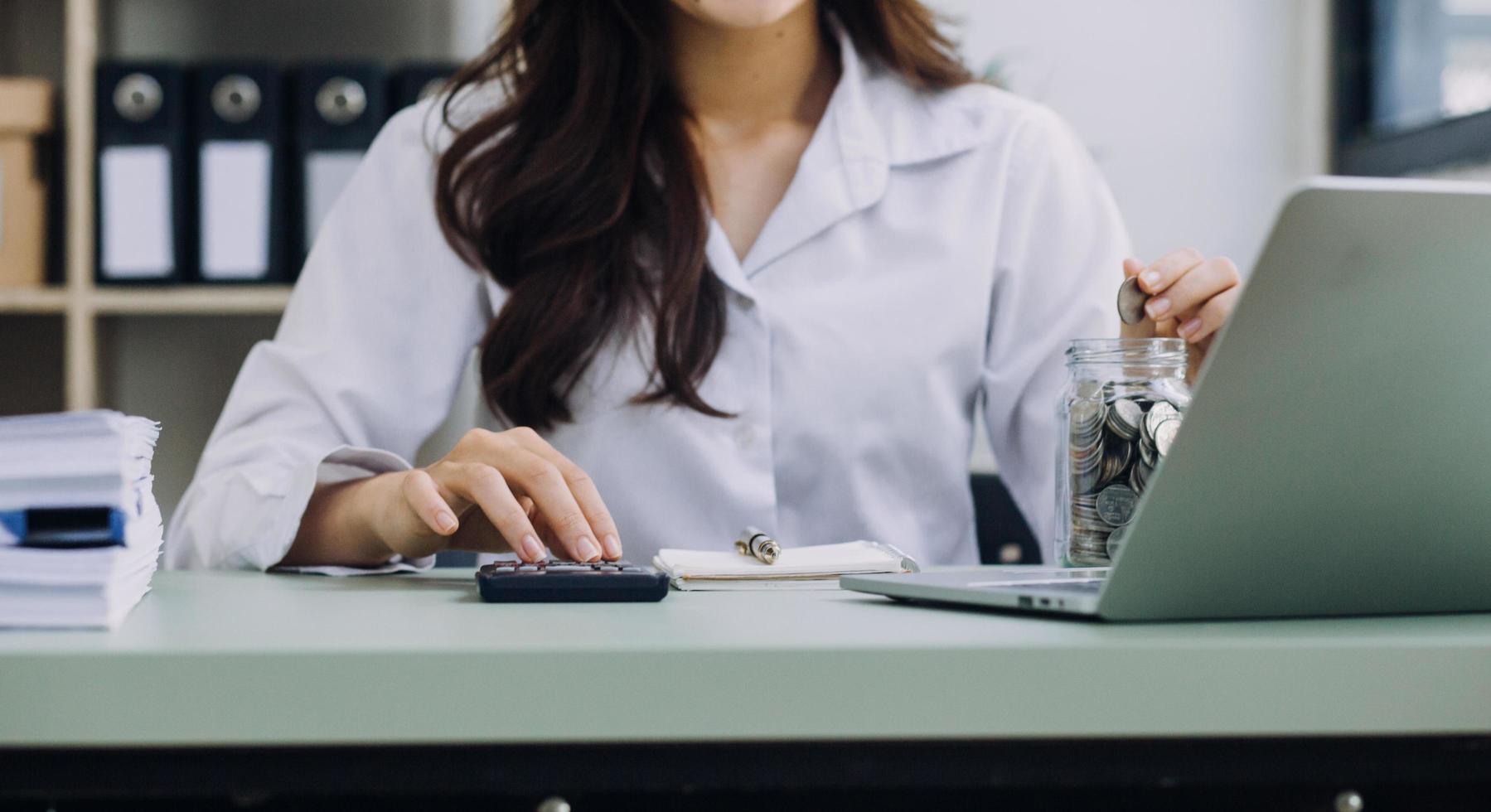 Young business woman sitting in office at table and using smartphone. On desk is laptop and tablet computer, on screen charts and graphs. Woman analyzing data. Student learning online. photo