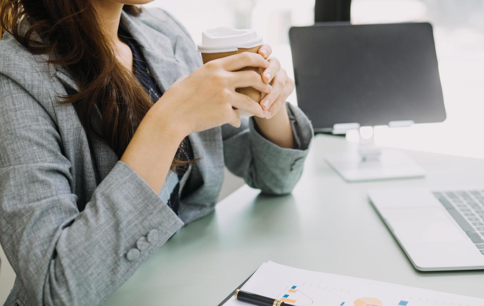 Young business woman sitting in office at table and using smartphone. On desk is laptop and tablet computer, on screen charts and graphs. Woman analyzing data. Student learning online. photo