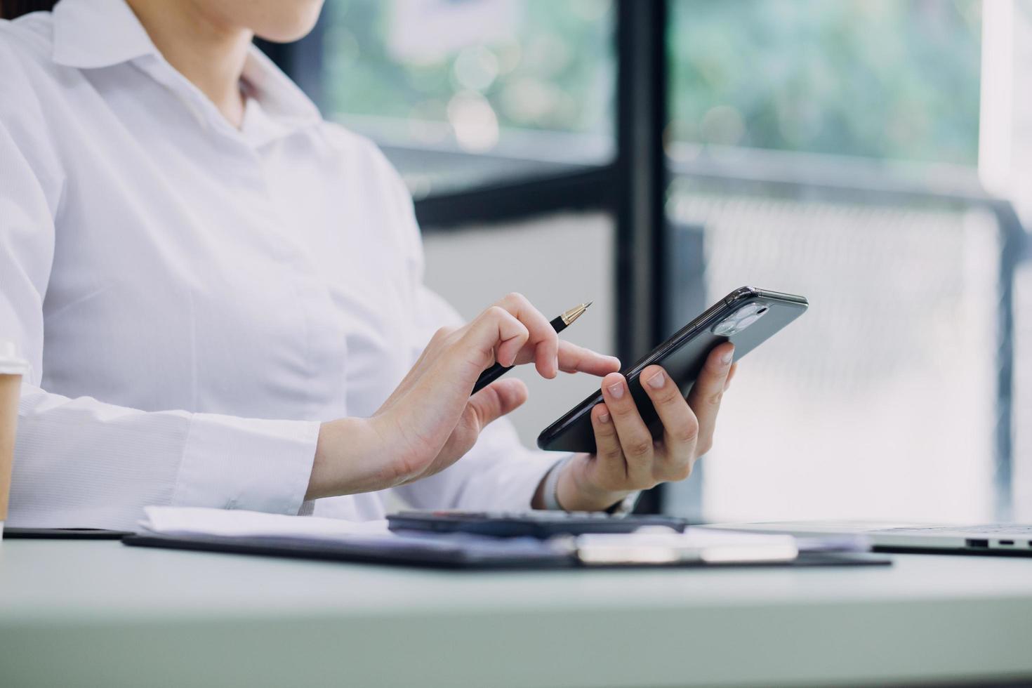 Young business woman sitting in office at table and using smartphone. On desk is laptop and tablet computer, on screen charts and graphs. Woman analyzing data. Student learning online. photo
