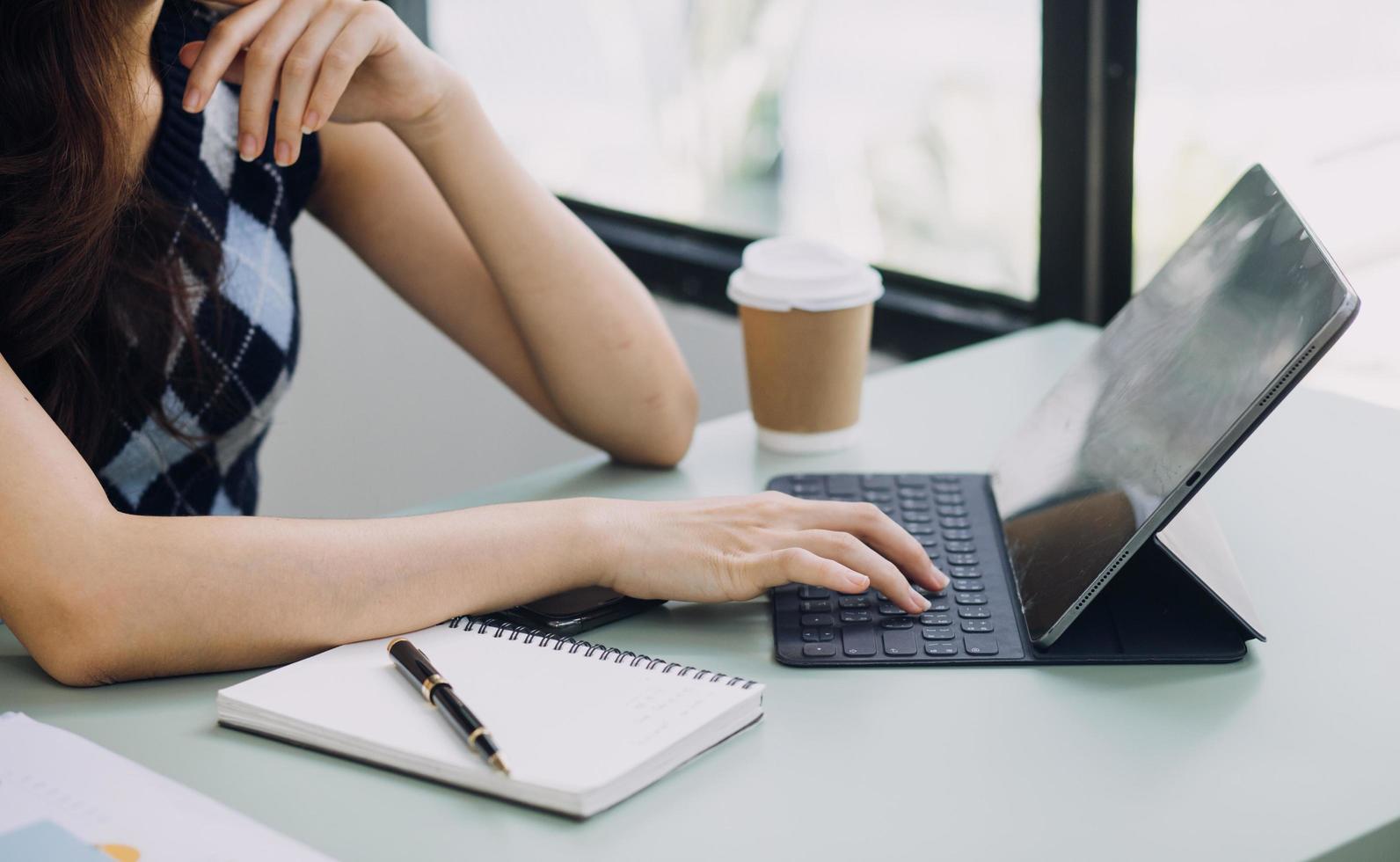 Young business woman sitting in office at table and using smartphone. On desk is laptop and tablet computer, on screen charts and graphs. Woman analyzing data. Student learning online. photo