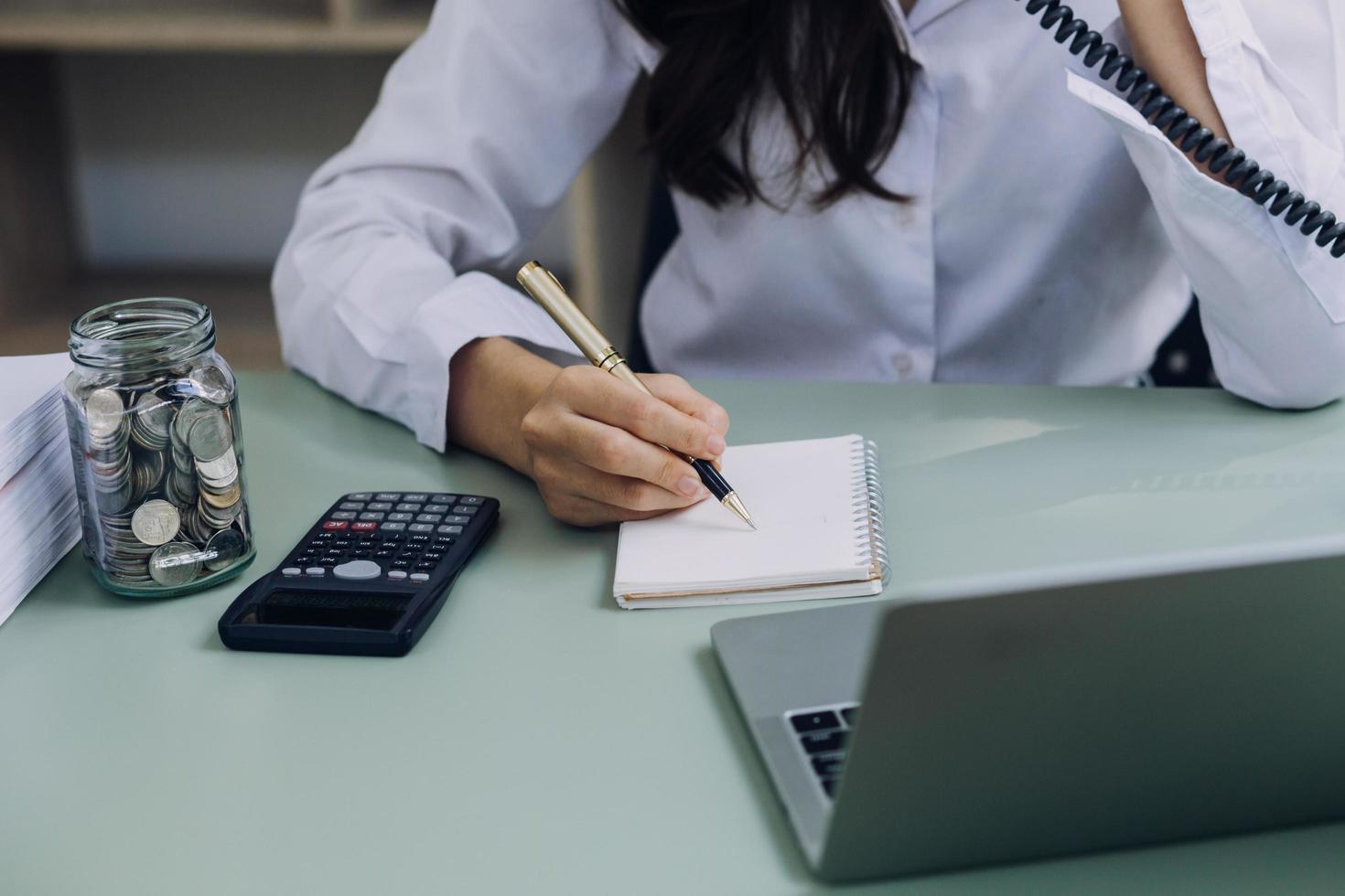 Young business woman sitting in office at table and using smartphone. On desk is laptop and tablet computer, on screen charts and graphs. Woman analyzing data. Student learning online. photo