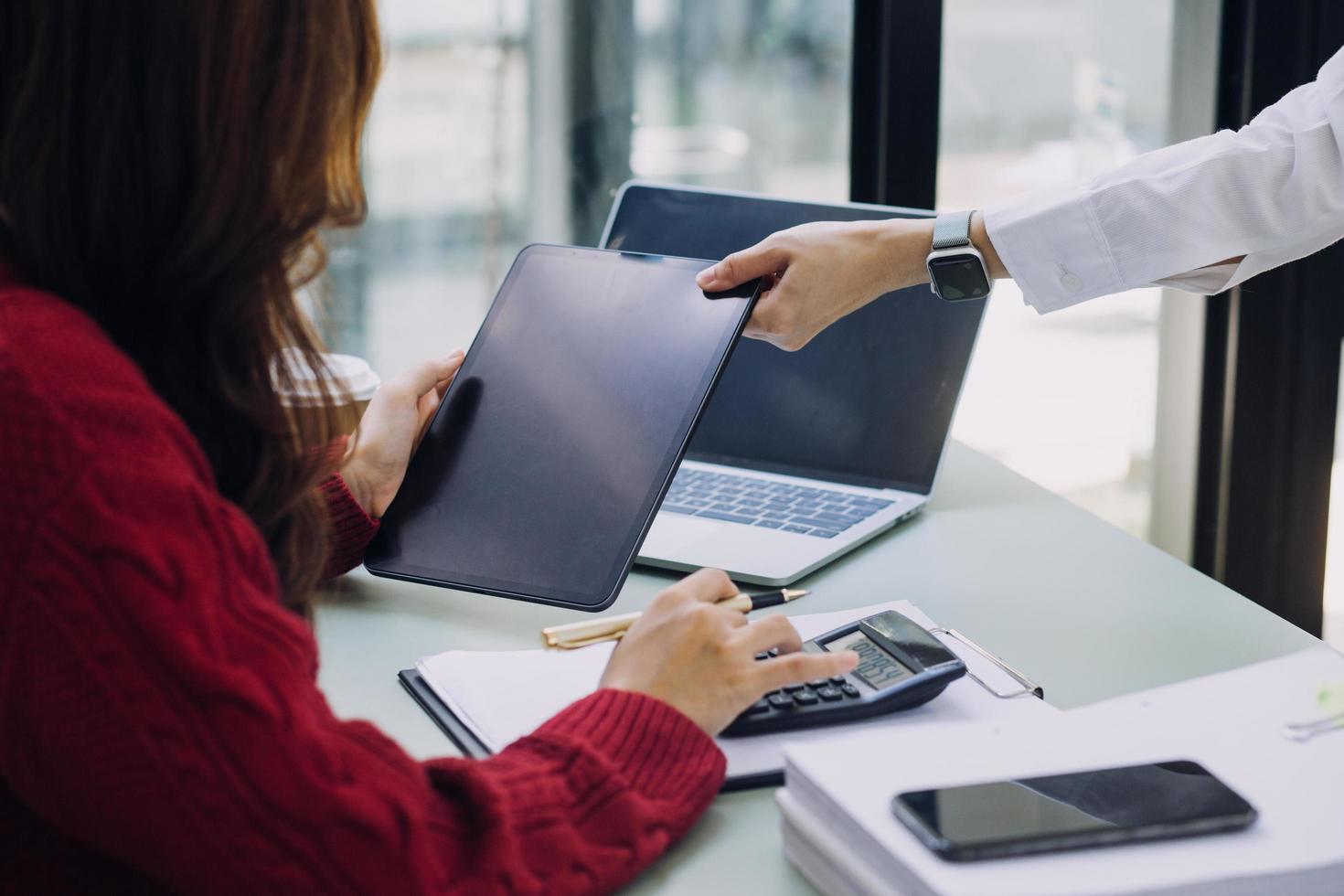 Young business woman sitting in office at table and using smartphone. On desk is laptop and tablet computer, on screen charts and graphs. Woman analyzing data. Student learning online. photo