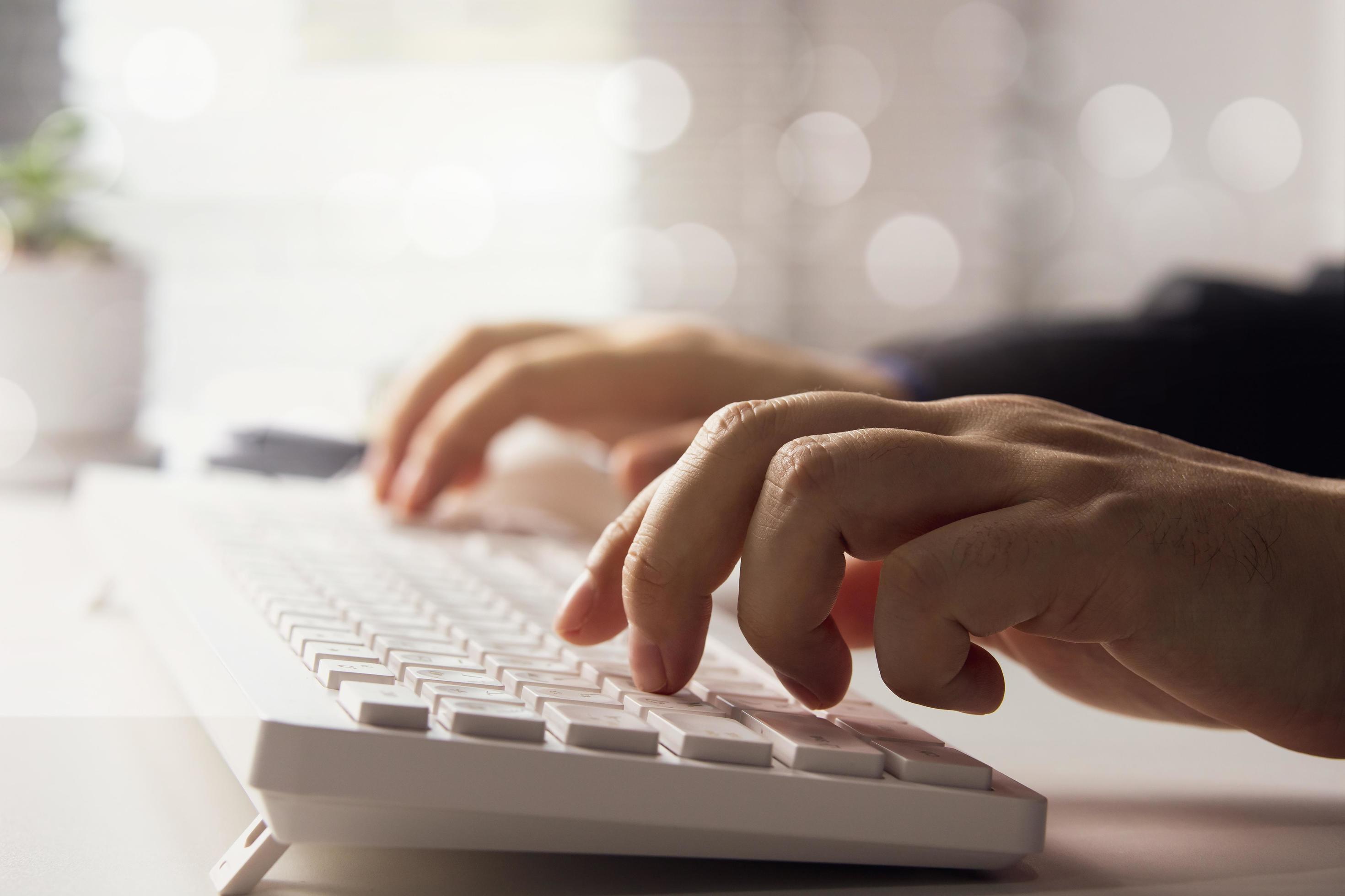 side view man hands typing computer keyboard White laptop on desk with