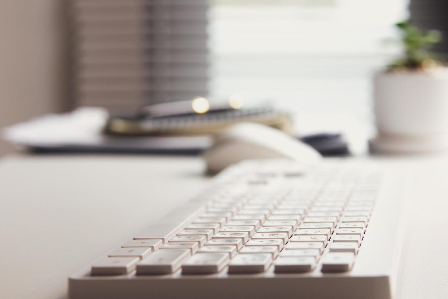 Side view of white keyboard on desk with blur light illuminating window in office. office workspace, freelance office corner photo