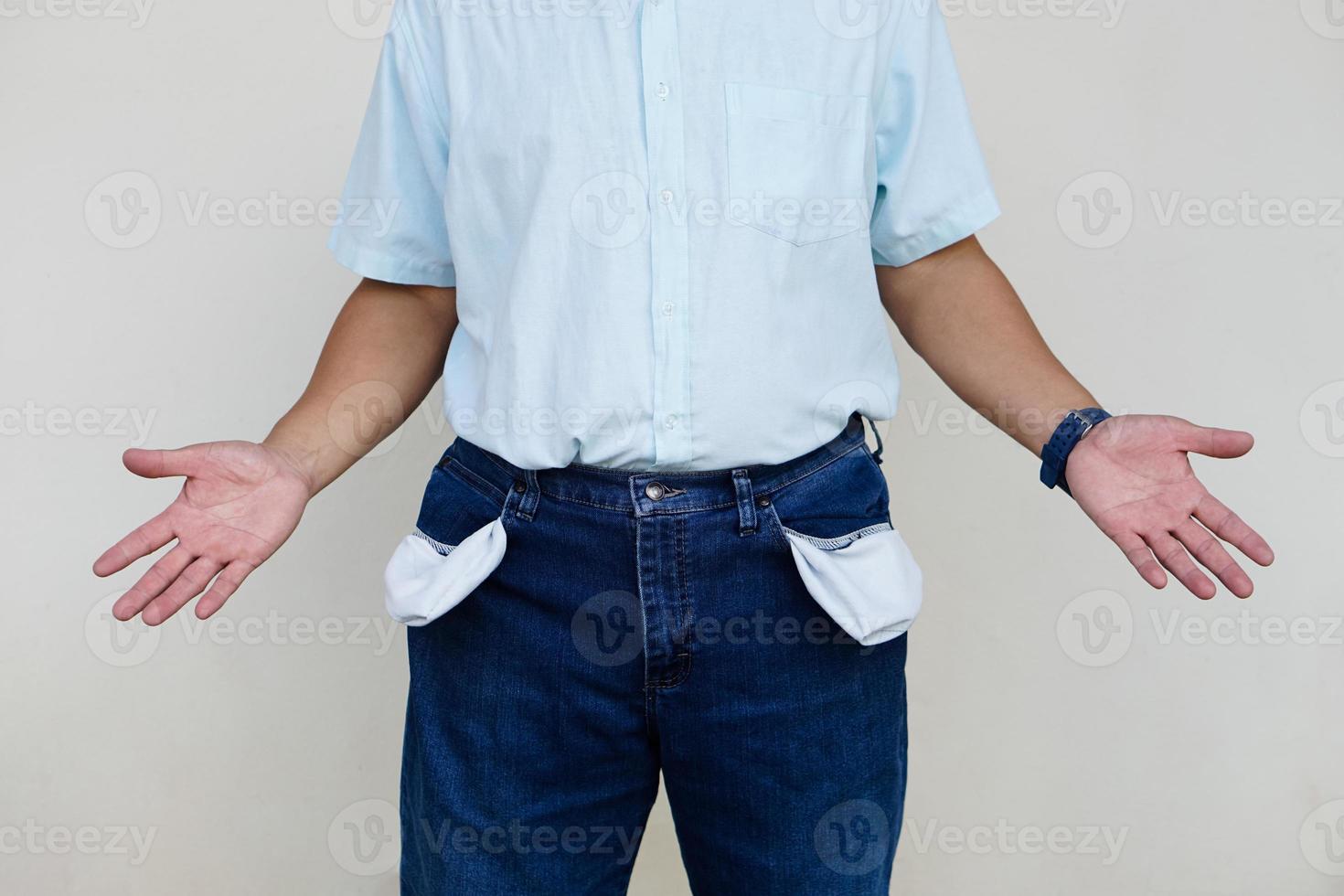 Man wears jeans, turning out  pockets to show empty pocket. Make hands gesture to show no money. Concept,  economic crisis. Financial problems. Broke at the end of month. Lost money. photo