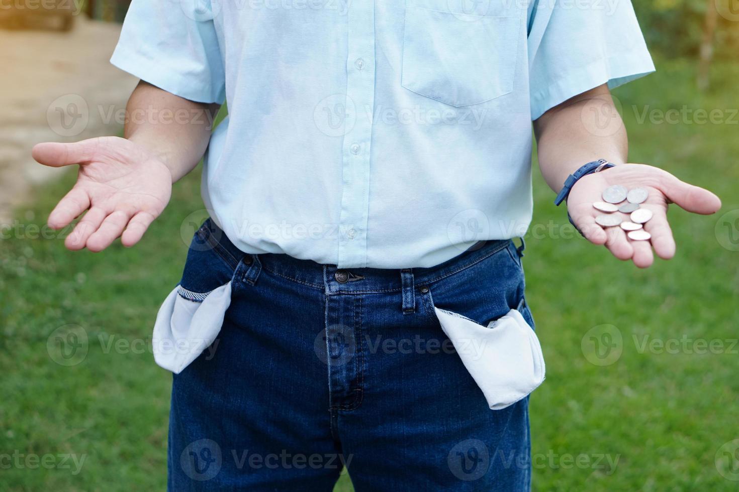 Closeup man wears jeans, turning out  pockets to show empty pocket. Make hands gesture to show few coins money. Concept, no money, economic crisis. Financial problems. Broke or less money. photo