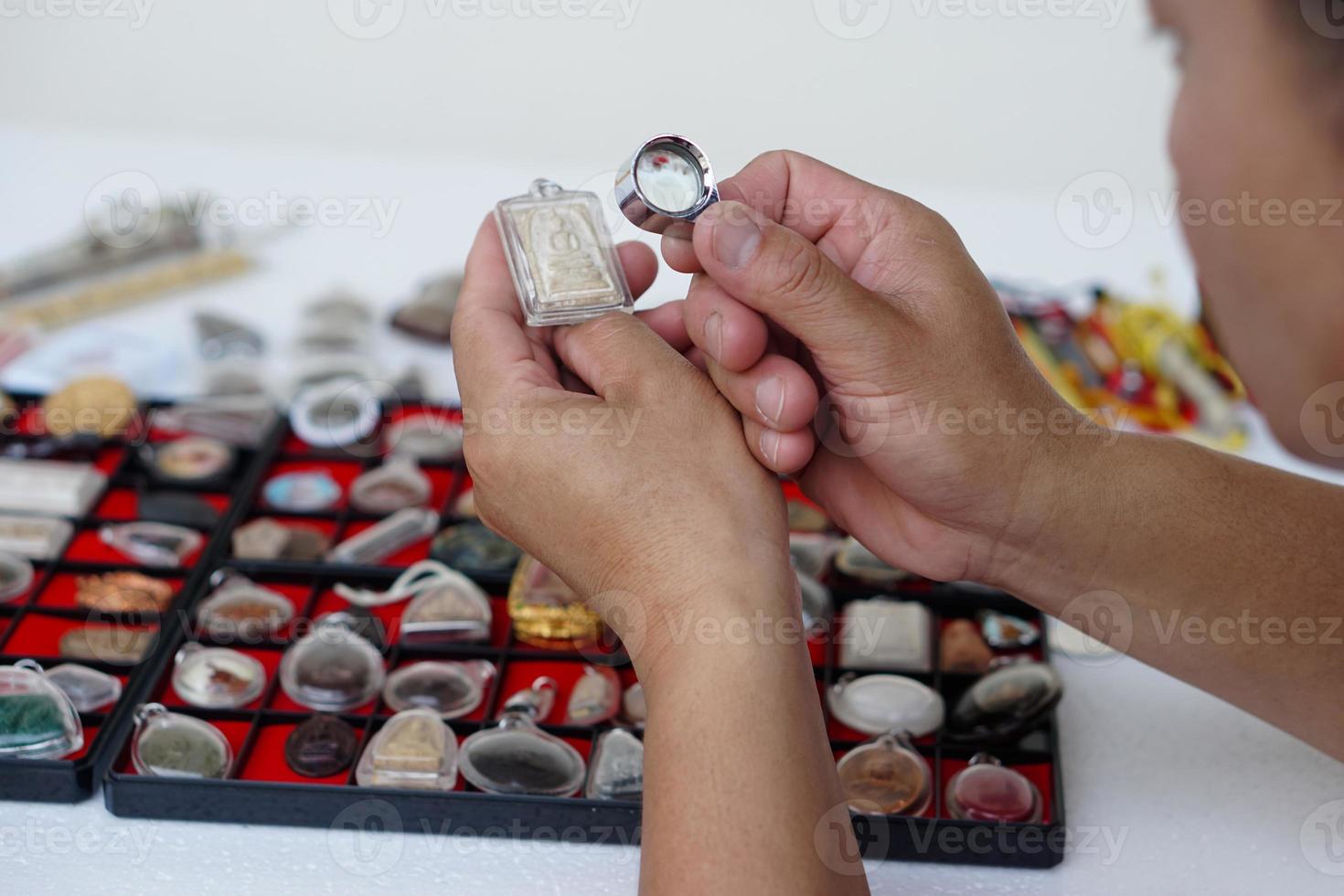 Closeup hands hold Buddha amulet and magnifying glass to check details and figure of object. Concept, faith and belief for Buddhist for holy and luck. Colleting amulet as hobbies, exchange, selling. photo