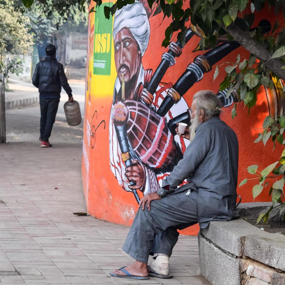 New Delhi, India - December 25, 2021 - Old poor man drinking tea during the winter season in old street of Delhi, Delhi Street Photography photo