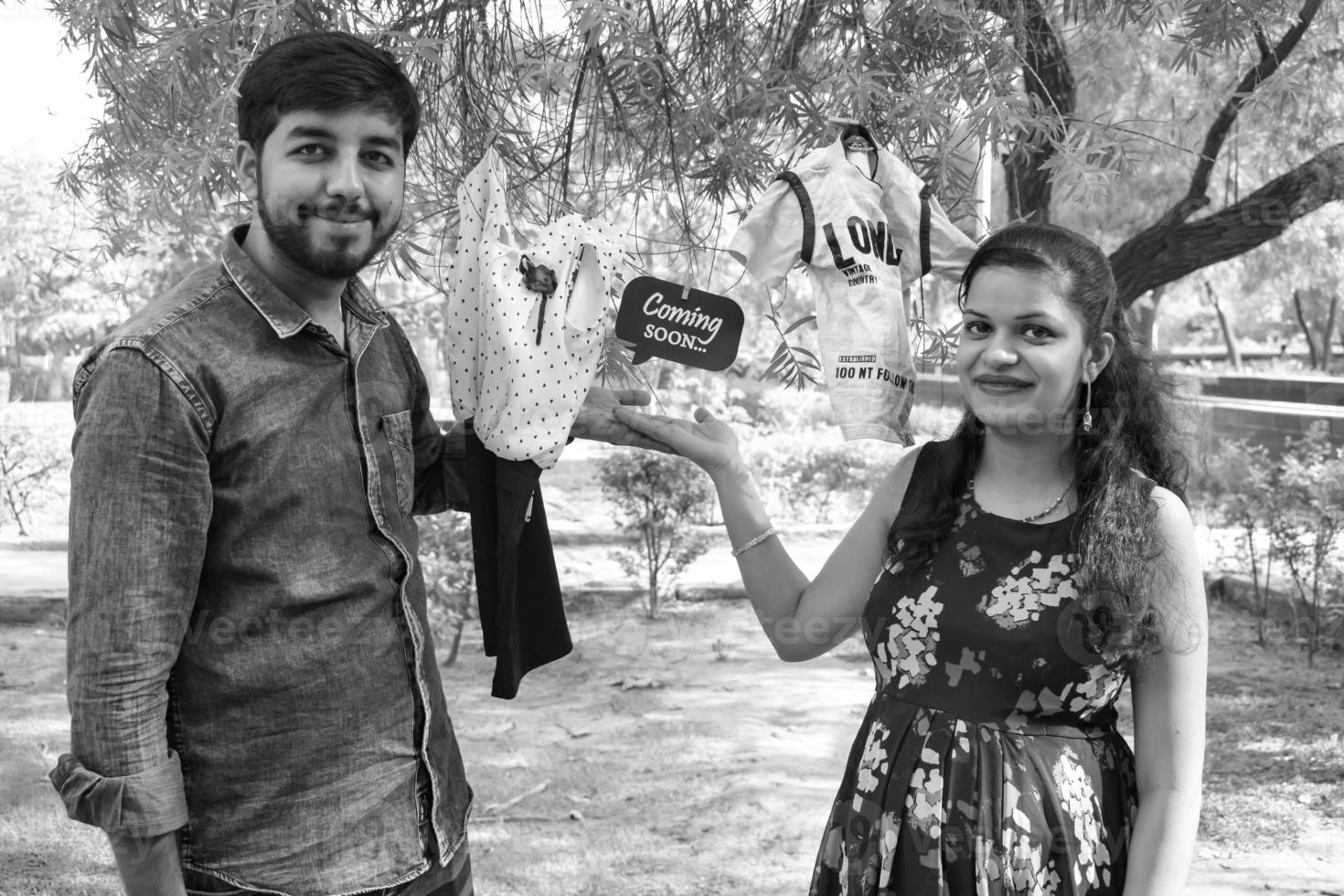 Indian couple posing for maternity baby shoot. The couple is posing in a lawn with green grass and the woman is falunting her baby bump in Lodhi Garden in New Delhi, India - Black and White photo