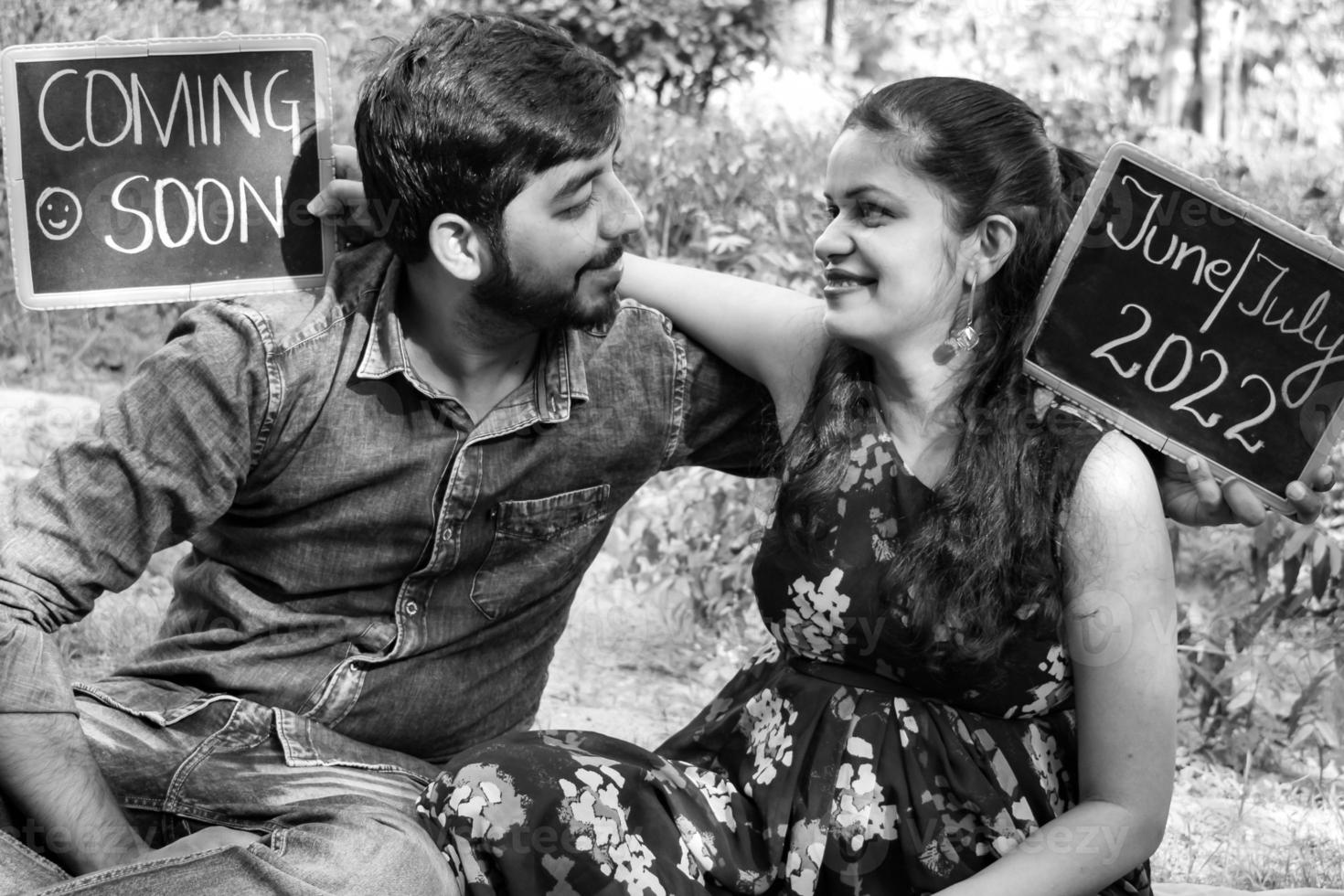 Indian couple posing for maternity baby shoot. The couple is posing in a lawn with green grass and the woman is falunting her baby bump in Lodhi Garden in New Delhi, India - Black and White photo