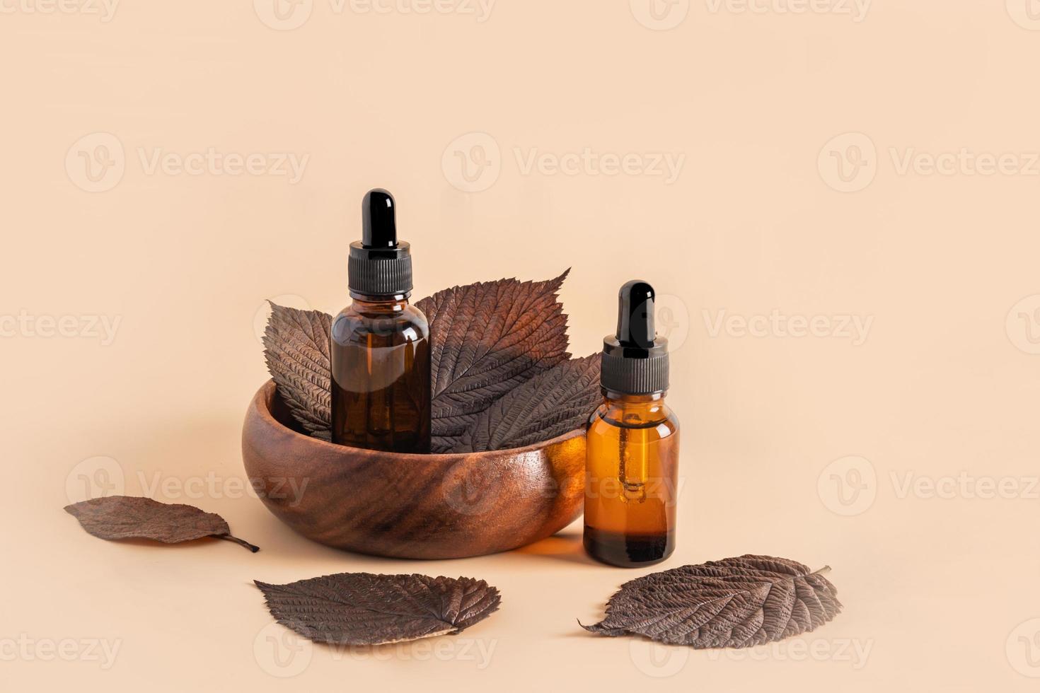 dos botellas cosméticas con una pipeta sobre un fondo beige y hojas marrones de otoño. cosmética natural para el cuidado de la piel del rostro. cuidado natural foto
