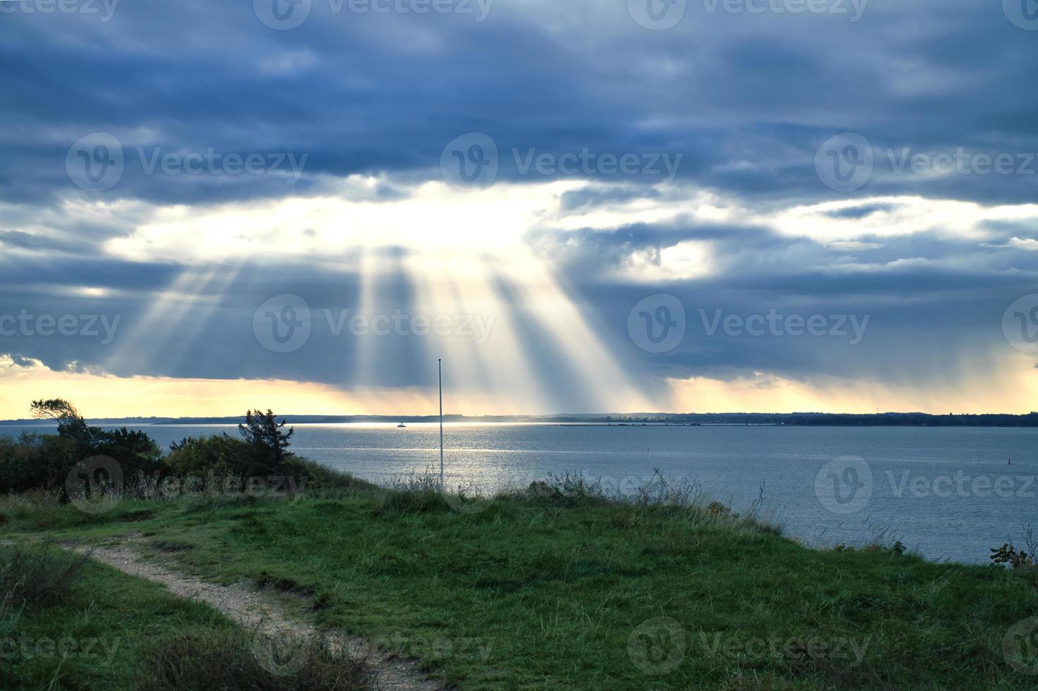 en la costa de hundested. los rayos del sol atraviesan el cielo dramático a través de las nubes foto