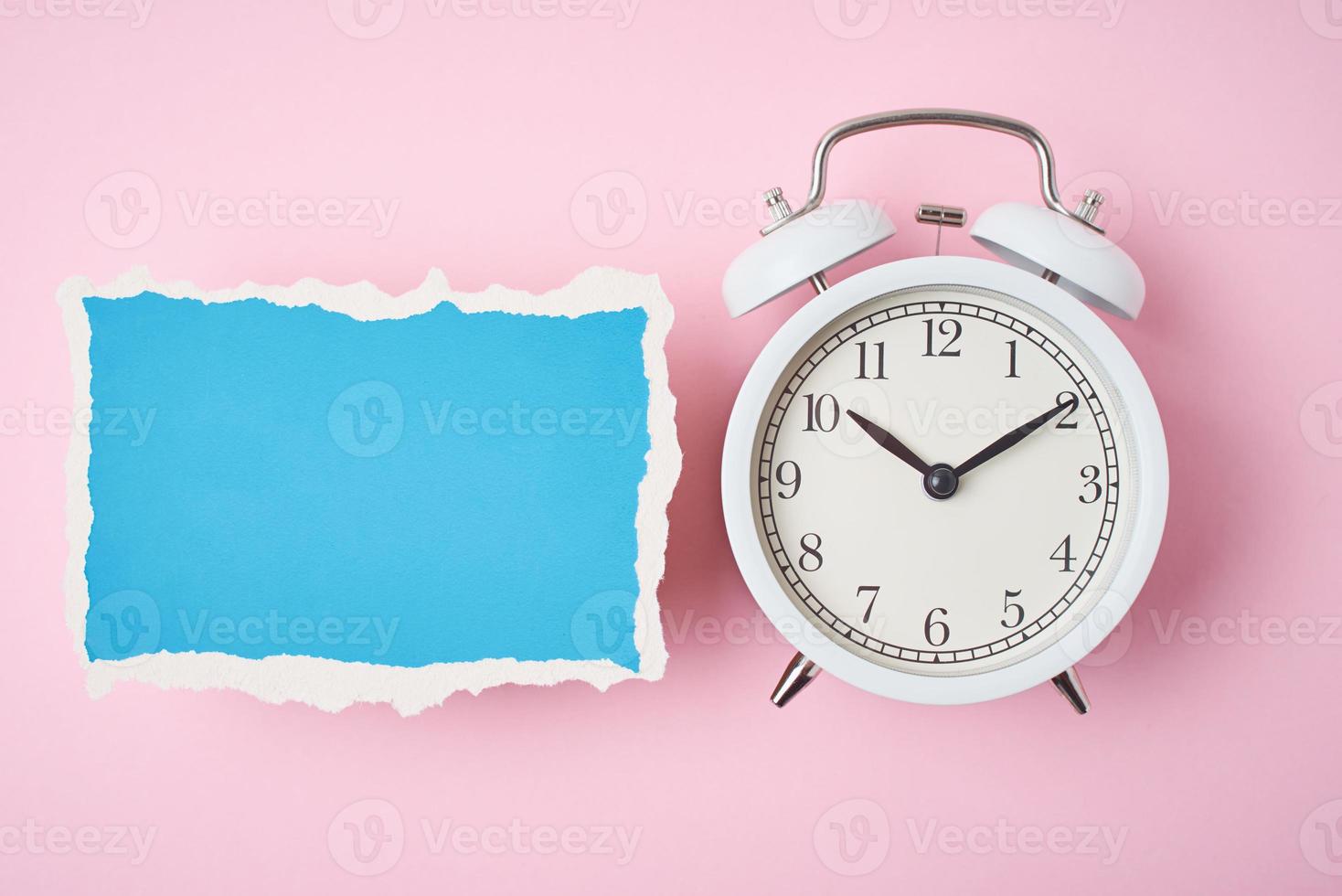 White alarm clock and empty torn paper sheet on a pink background photo