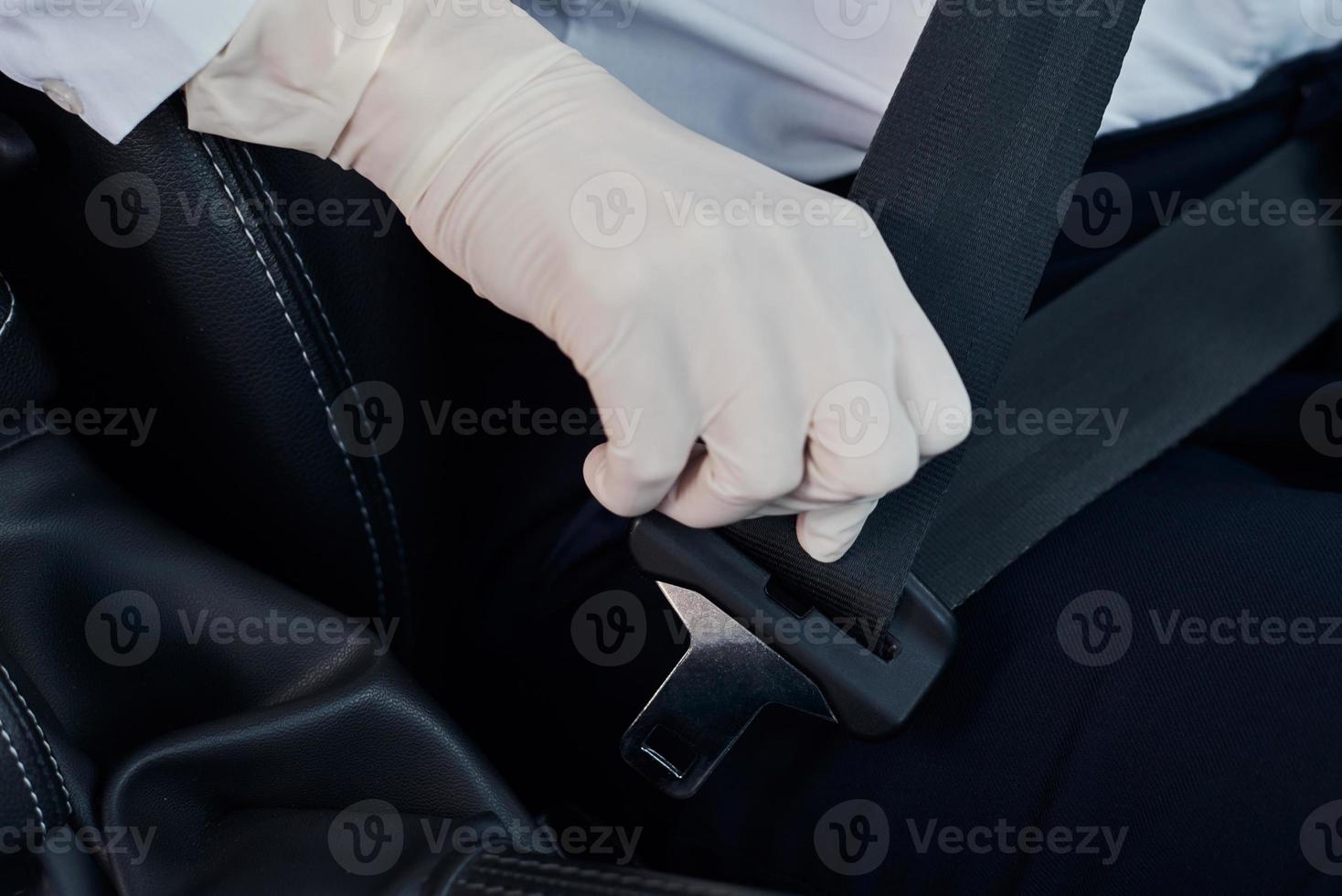 Driver in rubber gloves fastens seat belt in the car photo