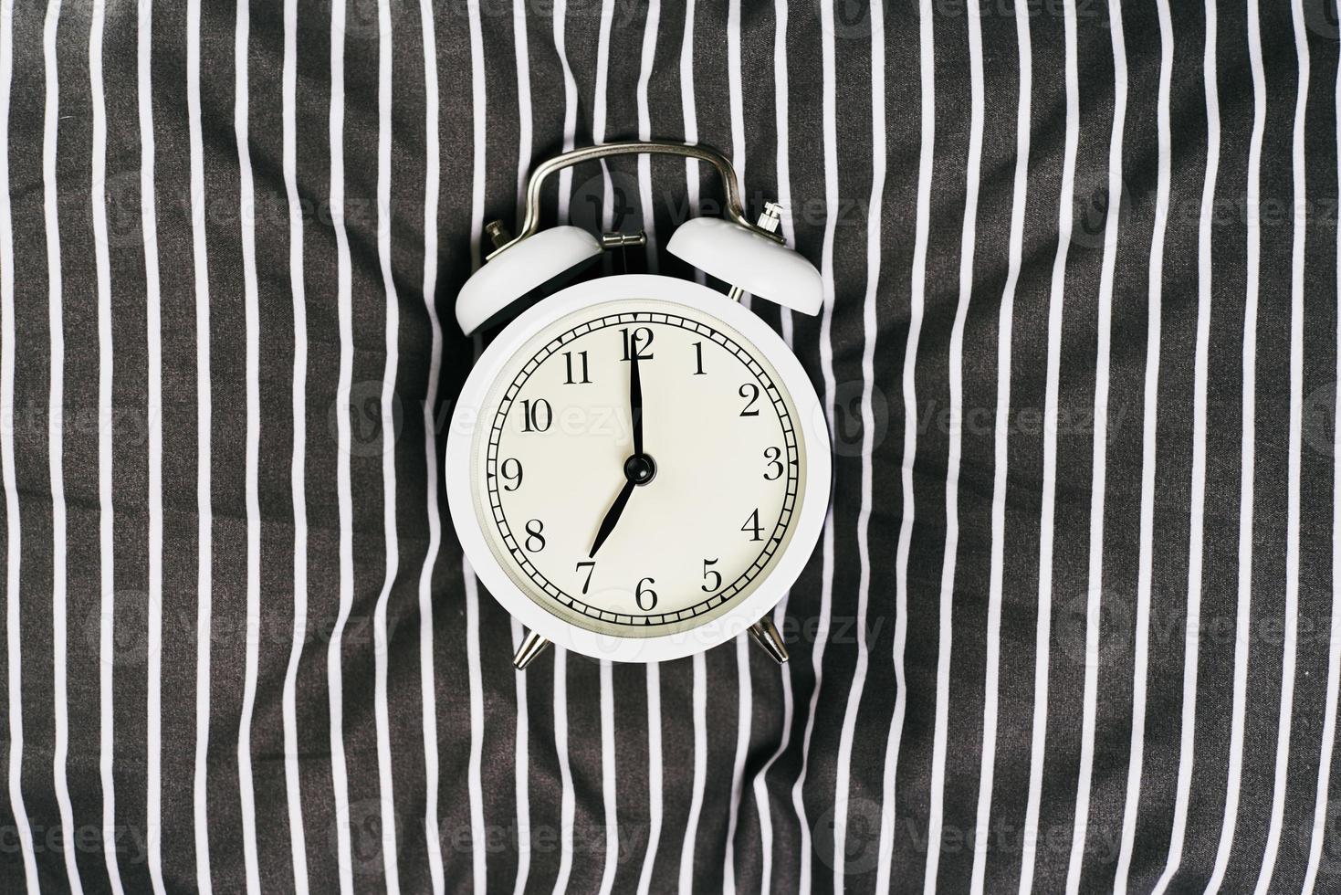 White vintage alarm clock on pillow in the bed. Wale up and morning concept photo