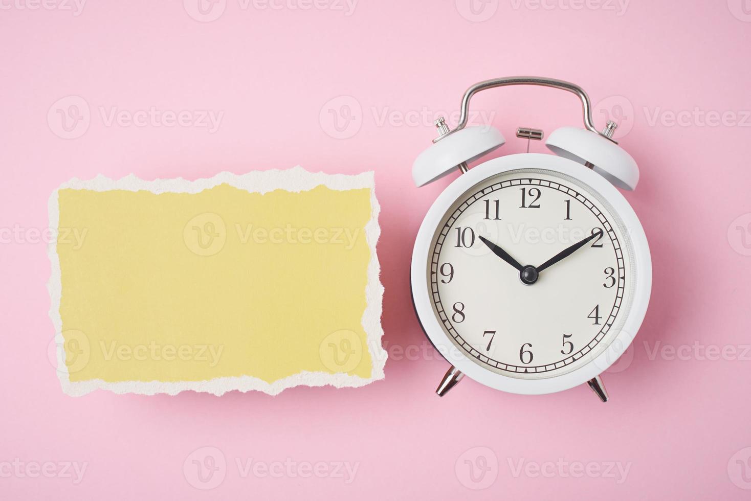 despertador blanco y hoja de papel rota vacía sobre un fondo rosa foto