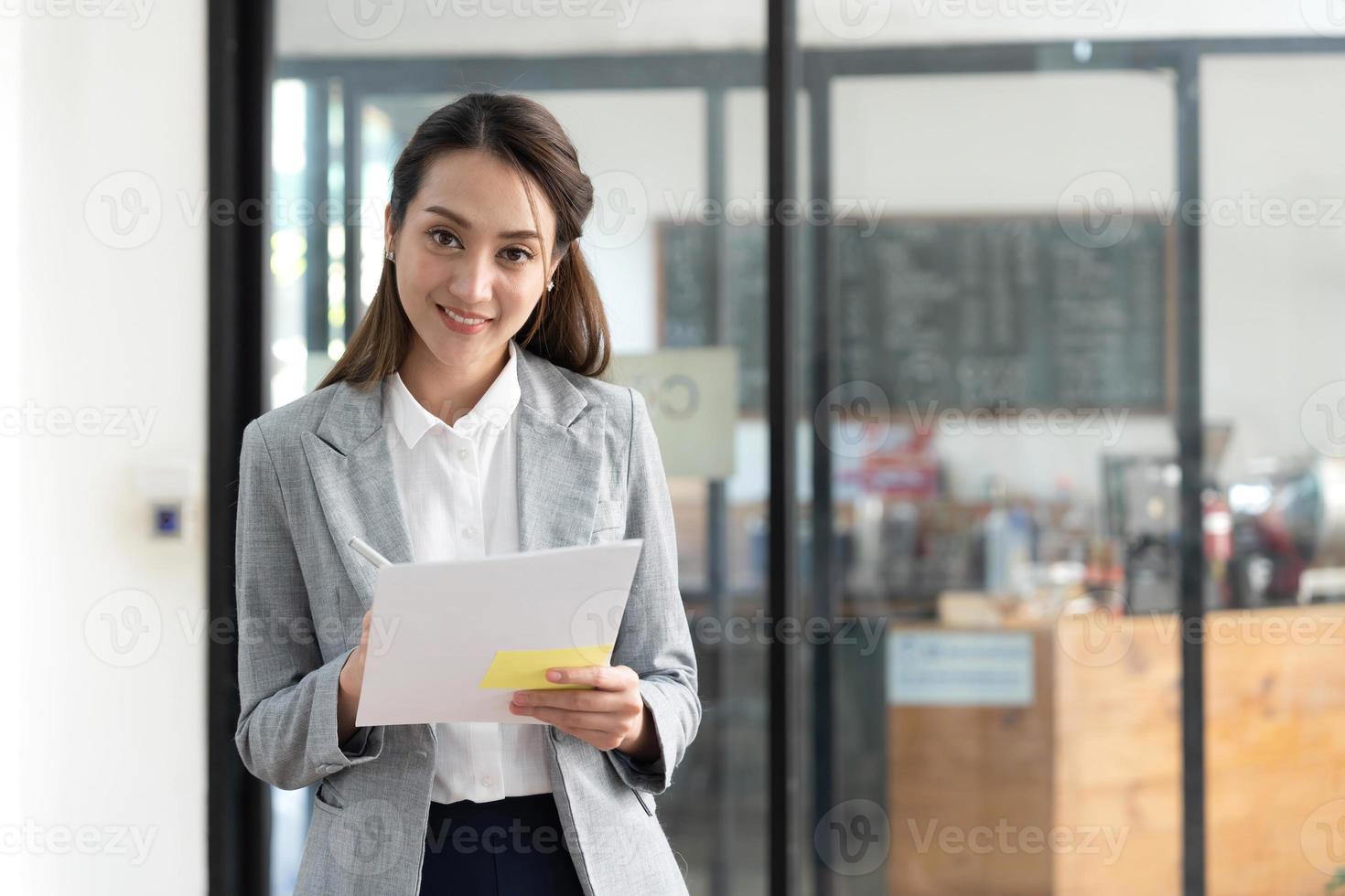 Charming young Asian businesswoman with a smile standing holding document clipboard at the office. Looking at camera. photo