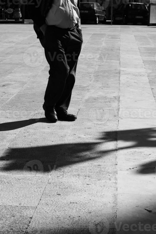 hombre siciliano en un cuadrado con las manos en los bolsillos con sombra alargada en blanco y negro.blanco y negro. sombra y luz, silueta de hombre foto