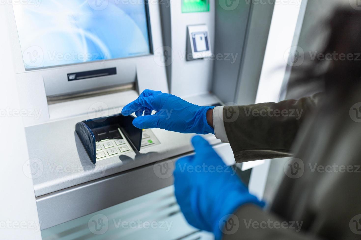 Young woman with protective mask and gloves standing on city street and using ATM machine to withdraw cash. Corona or Covid-19 virus pandemic concept. photo