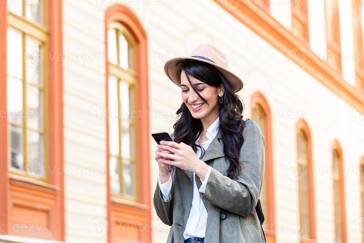 Photo of a woman using smart phone. Beautiful woman texting on the street. Beautiful woman spending time in the city. Fashionable woman with smart phone