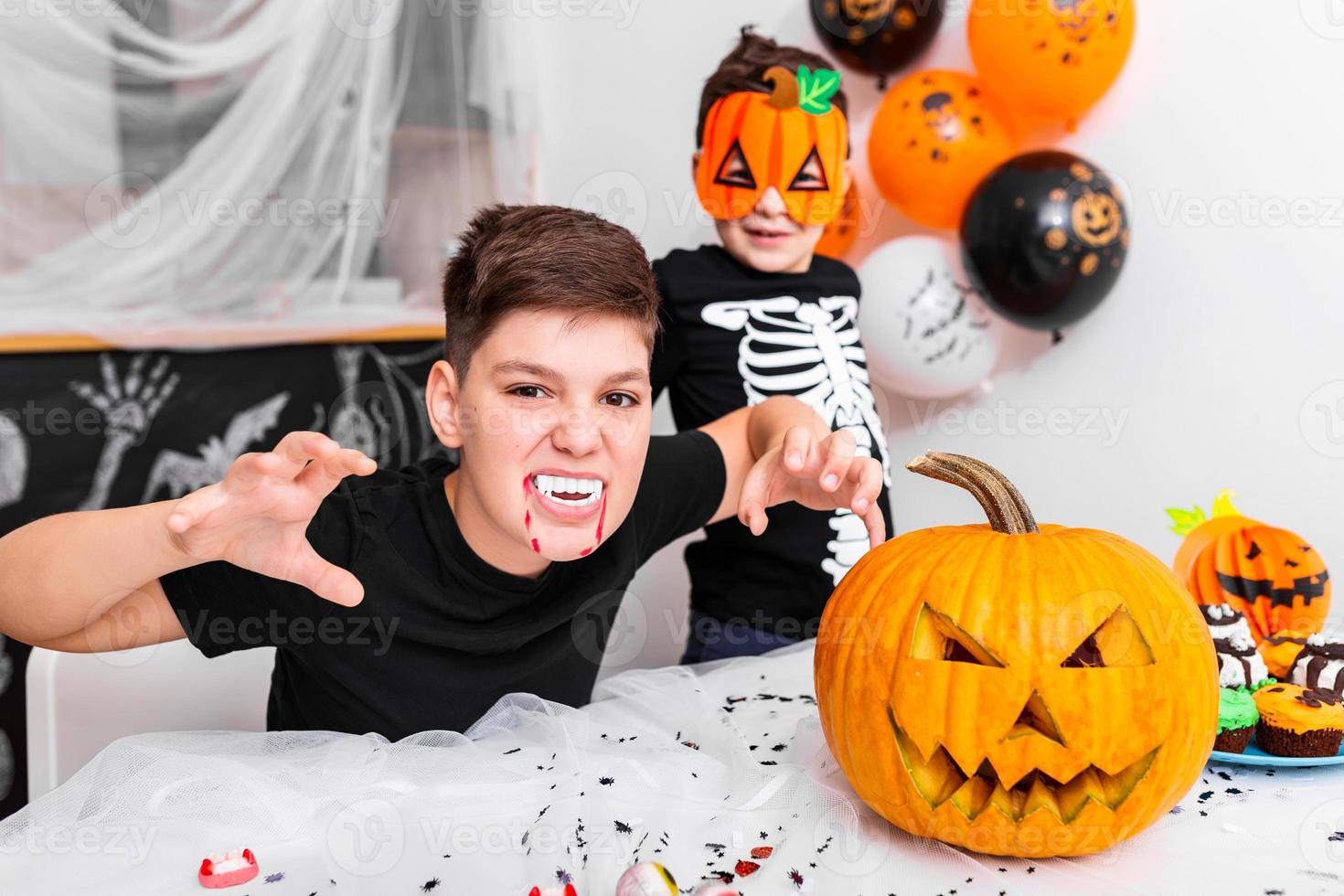 Scary boy with vampire fangs looking at the camera on thehalloween party. Jack O' Lantern Halloween pumpkin on the table photo