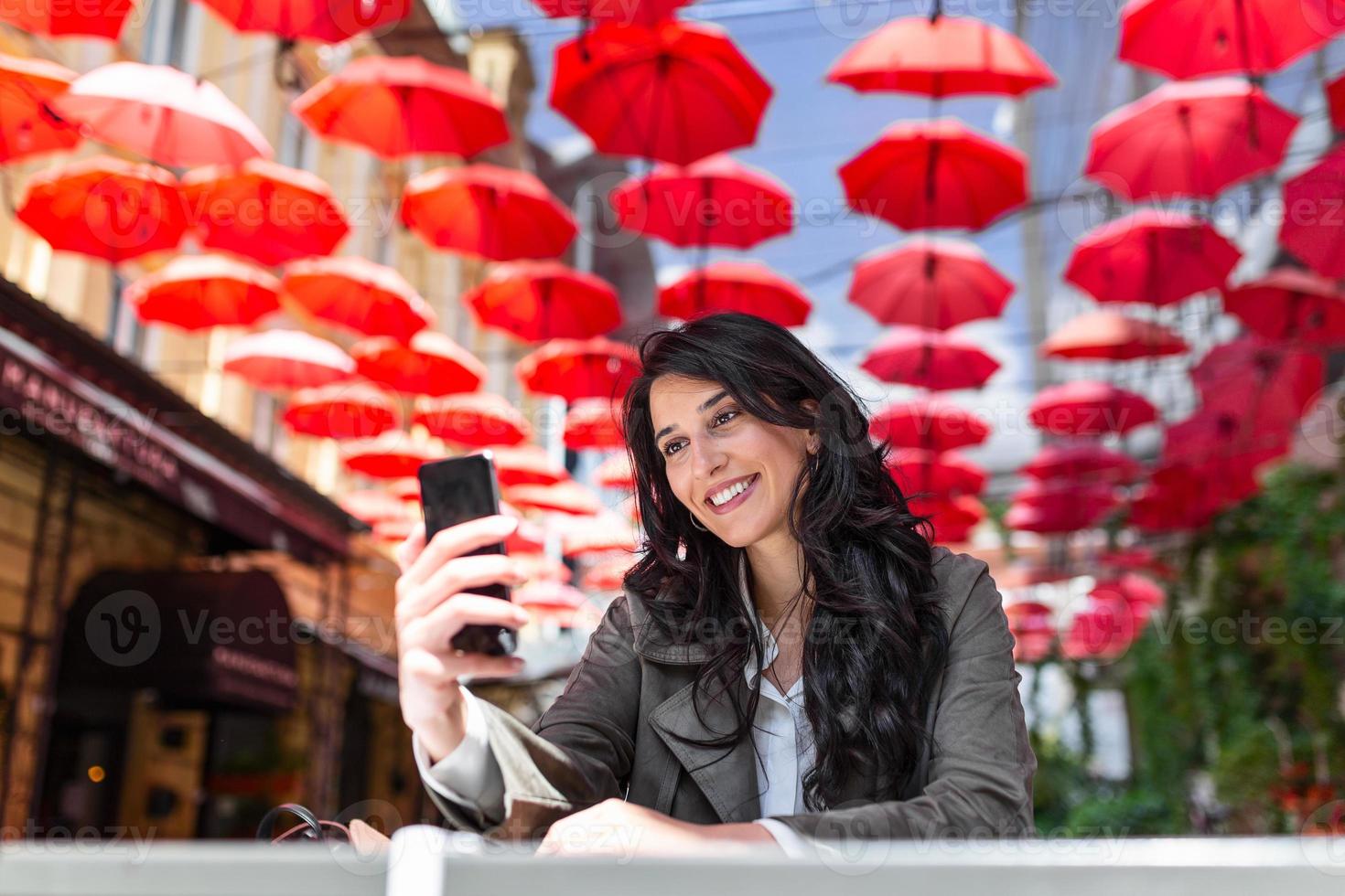 Smiling woman drinking coffee and using her mobile phone. Satisfied female enjoying cup of coffee. Close up portrait of beautiful girl drinking coffee and making a selfie photo
