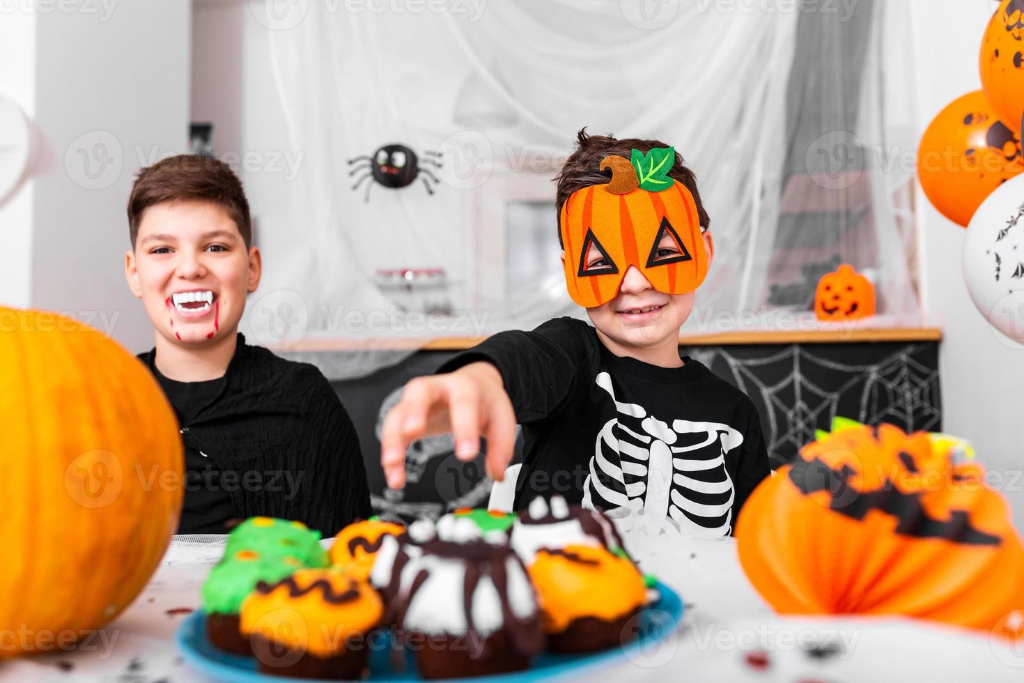 Happy Halloween Attractive young boy with his brother are preparing for Halloween party. Brothers in costumes are having fun with pumpkins and cupcakes. photo